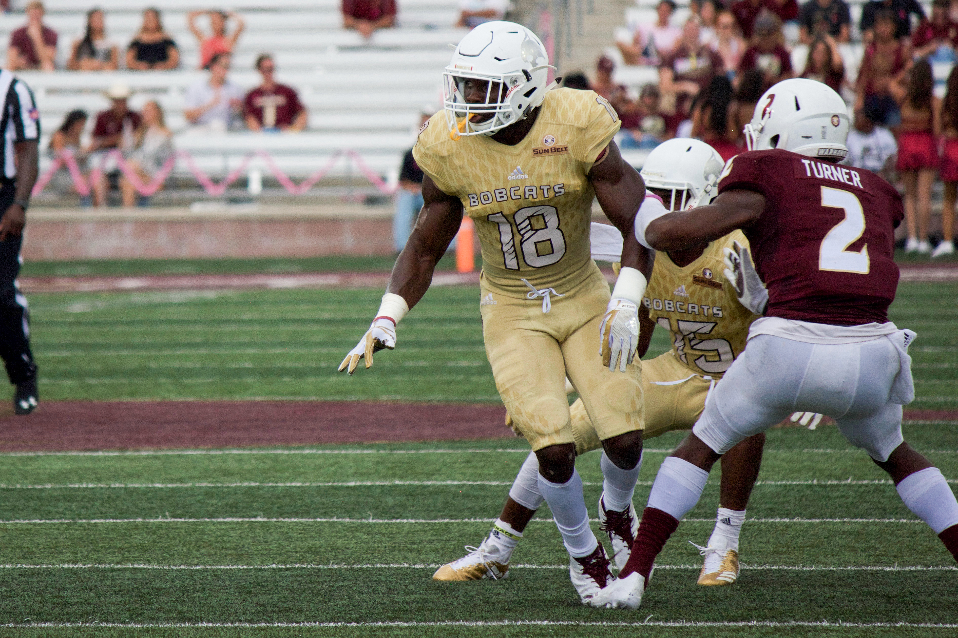 In a bright golden jersey, linebacker Frankie Griffin takes an aggressive step-forward against the night black jerseys of the University of Louisiana-Monroe. 