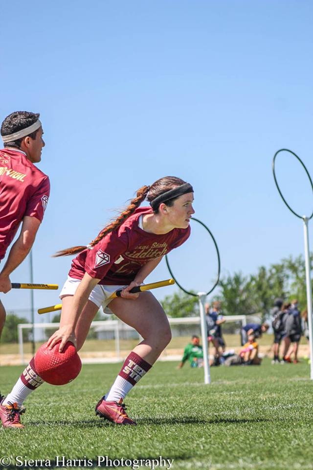 Female quidditch player reaching for dodgeball on Quidditch field