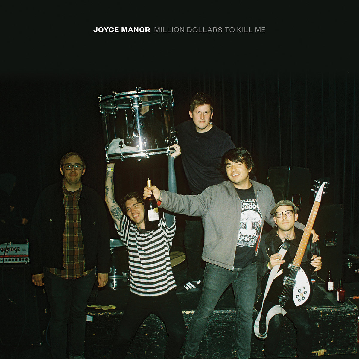 The band members, one holding up a drum, and their gear on a black background.