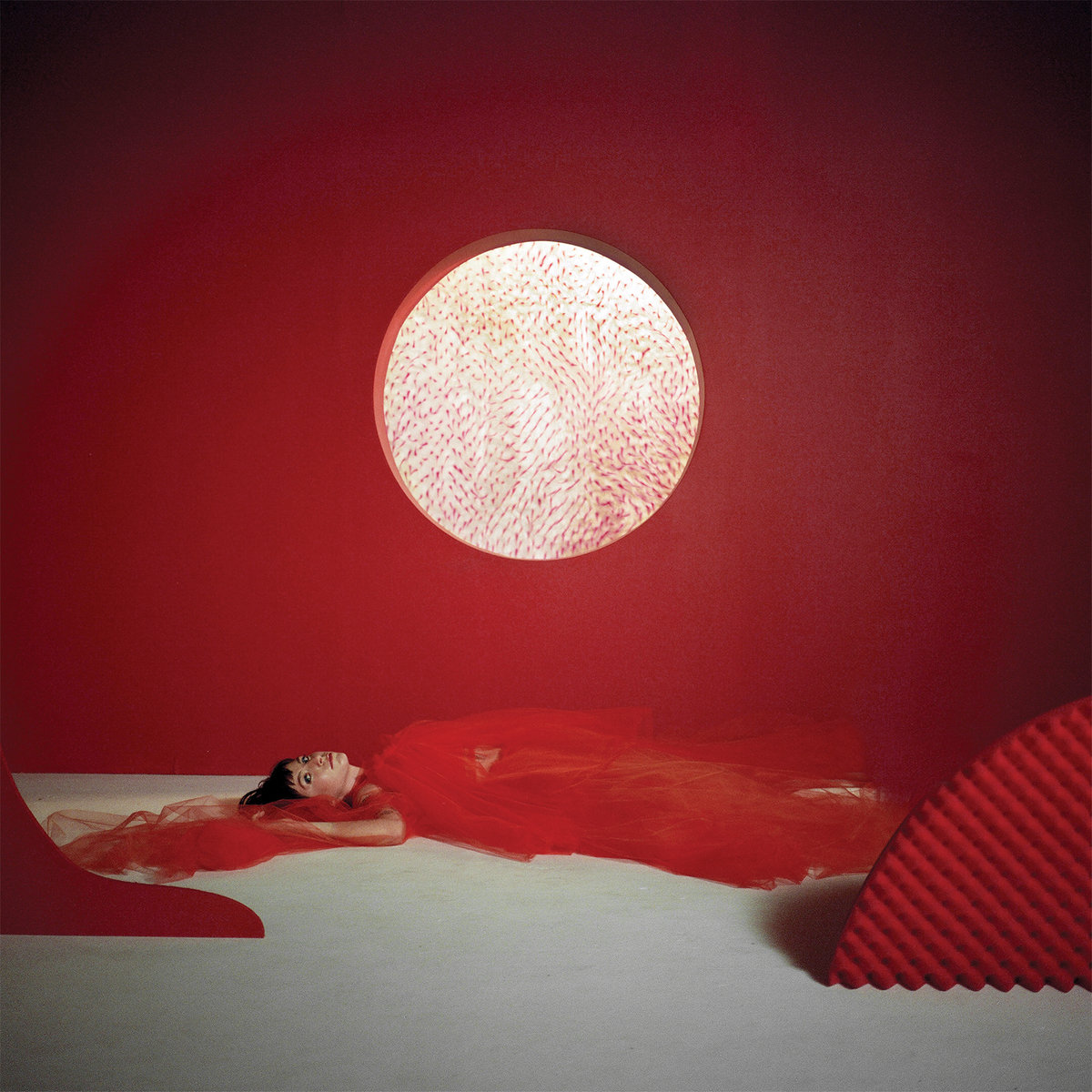A woman in red tulle lying on the ground with a red backdrop and white circle.
