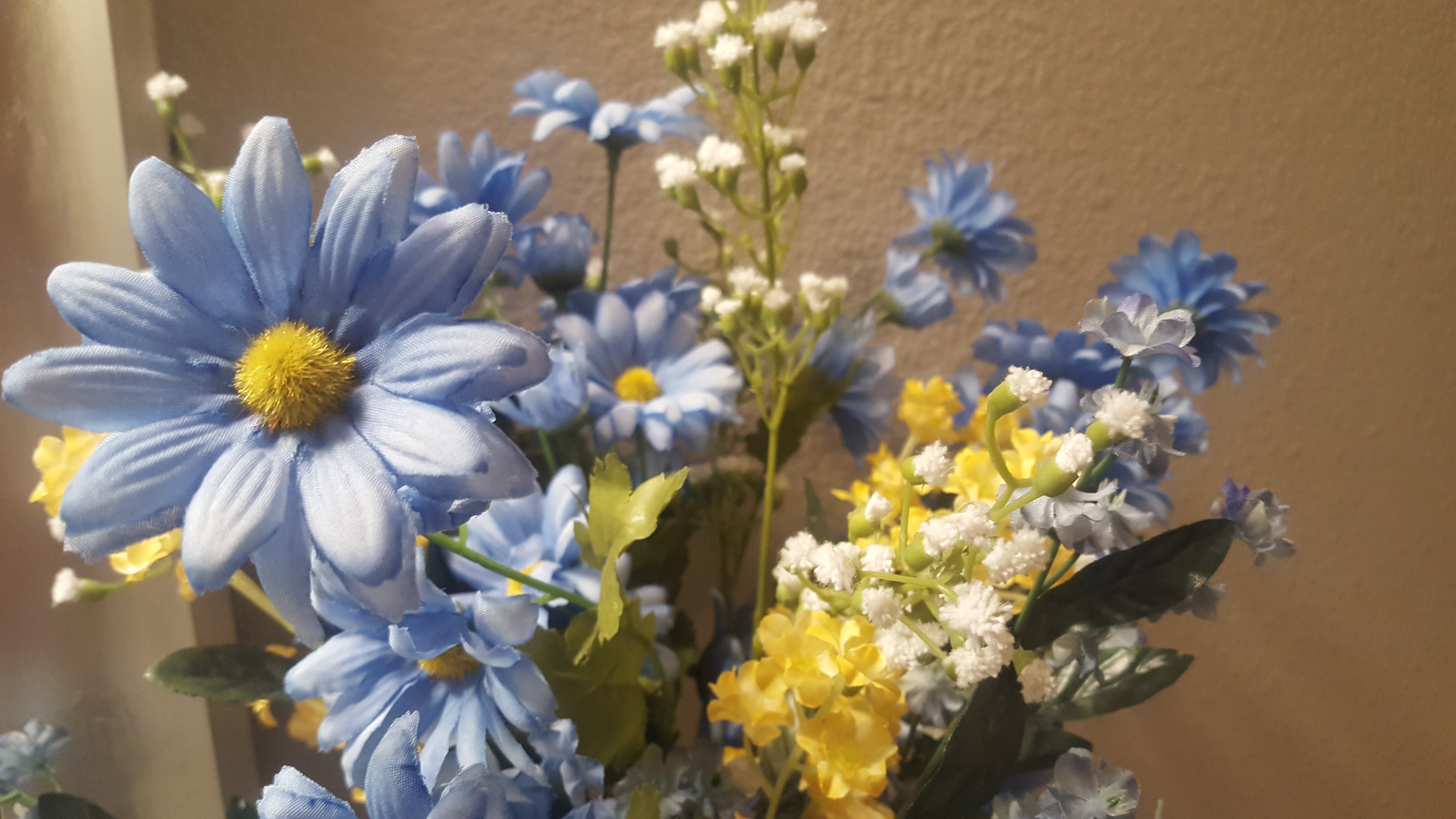 Bouquet with a mixed arrangement of blue, yellow and white flowers is sitting on a bathroom counter for decoration