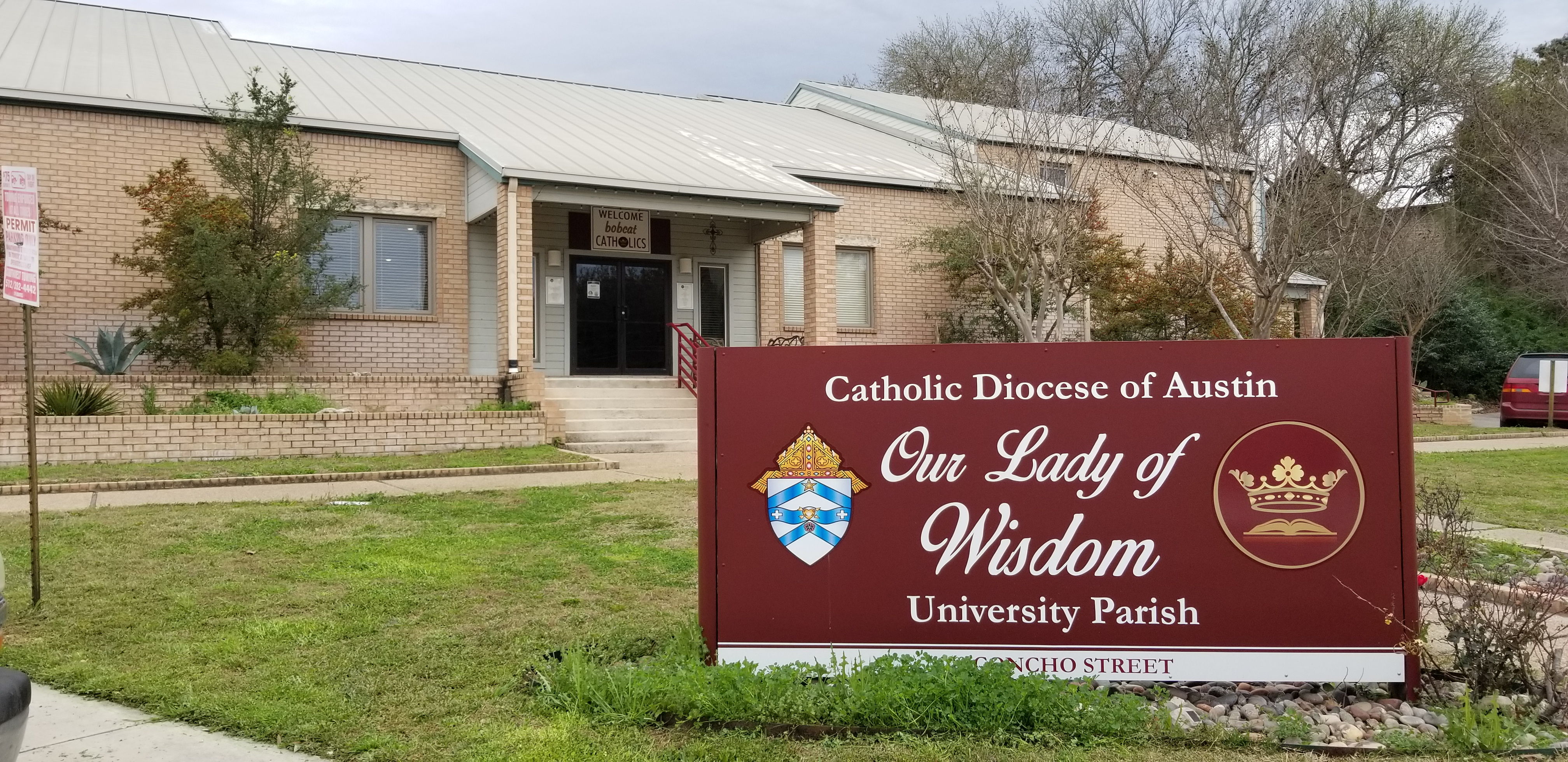 Front side of a church, with a sign that reads Catholic Diocese of Austin Our Lady of Wisdom University parish.