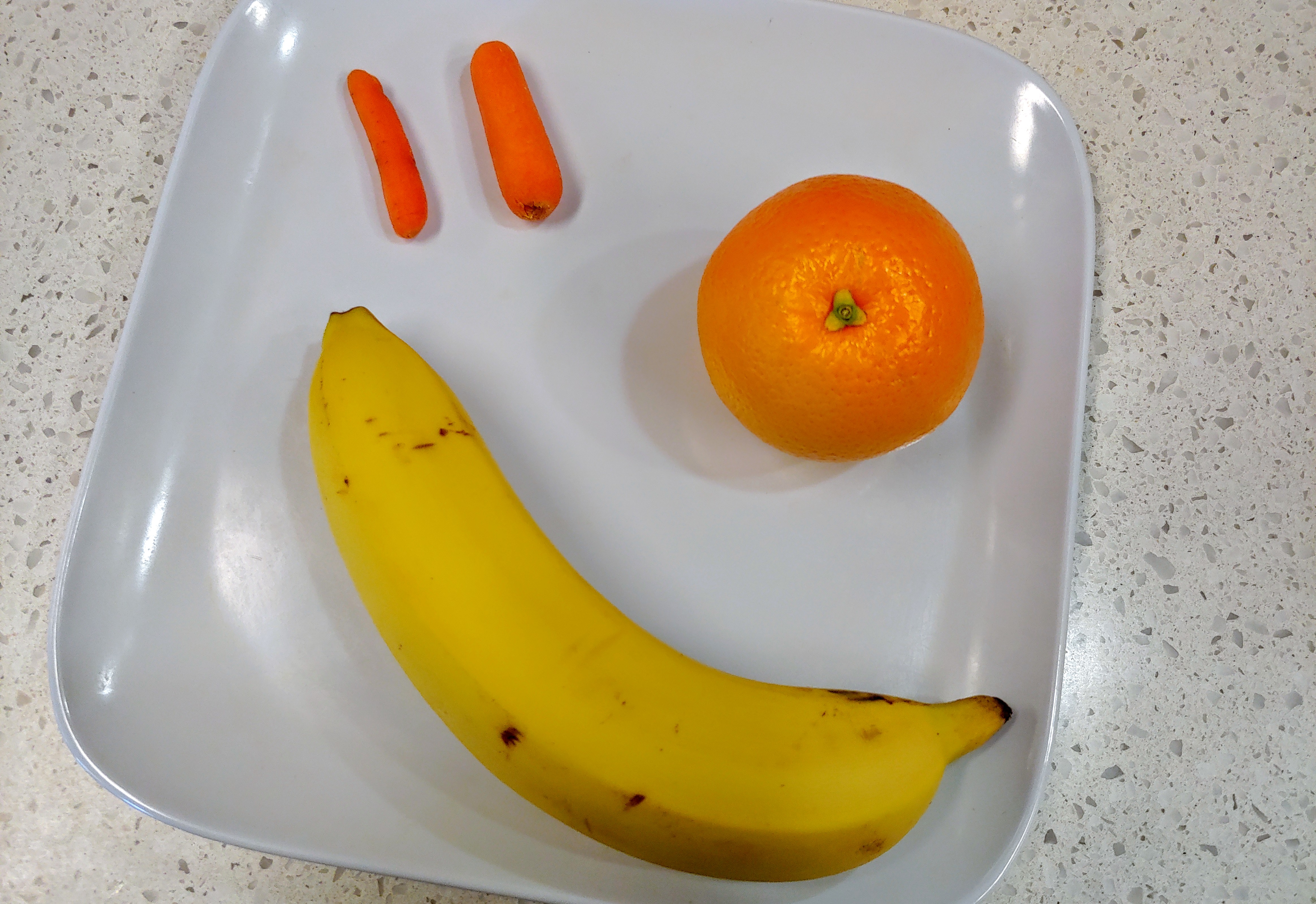 A picture of a plate of one banana, one orange, and two baby carrots.