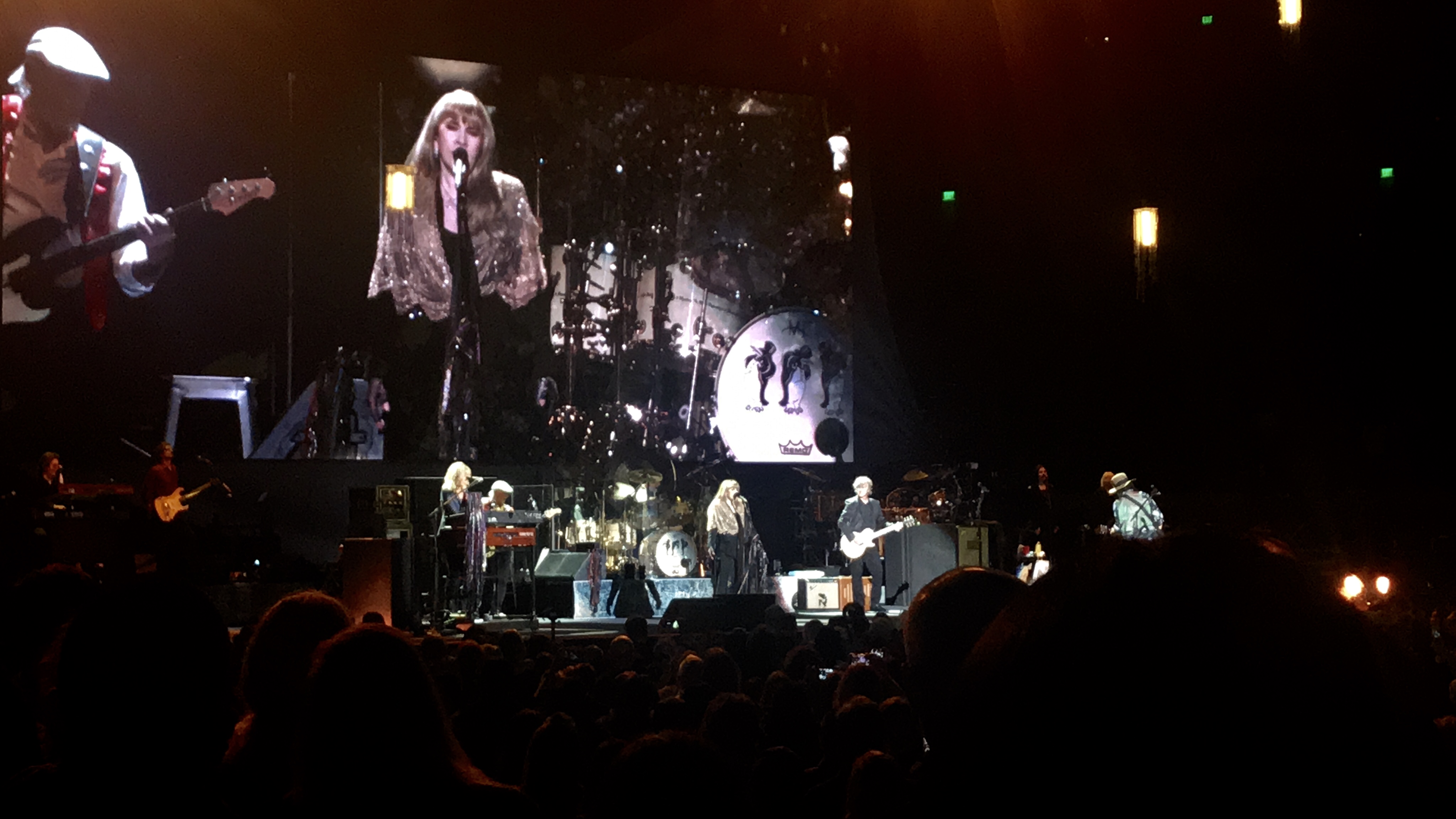 Stevie Nicks sings in the middle wearing a glittery gold shawl. Christine McVie and John McVie are to her left playing keyboard and bass, and Neil Finn and Mike Campbell her to her right playing guitar.