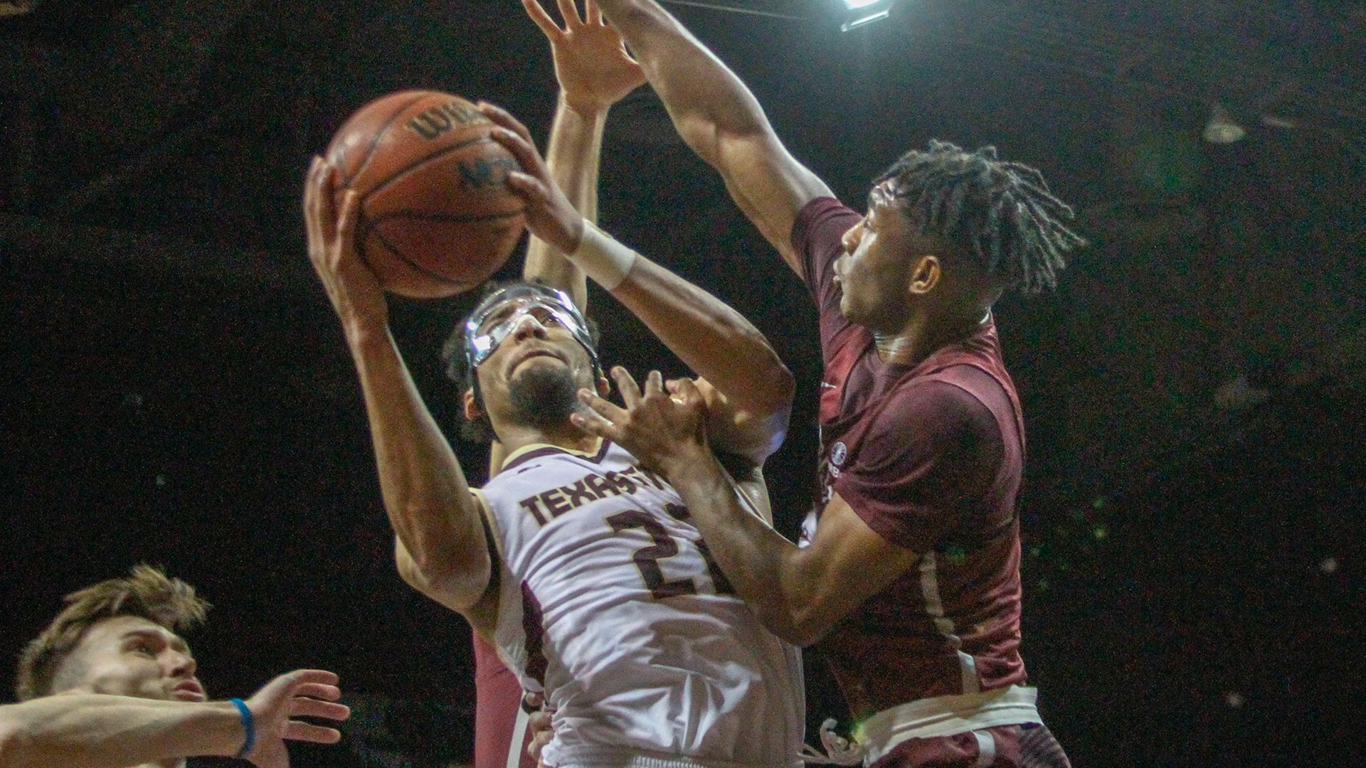 Basketball Player in white jersey goes up for a layup against another Basketball player in a maroon jersey.