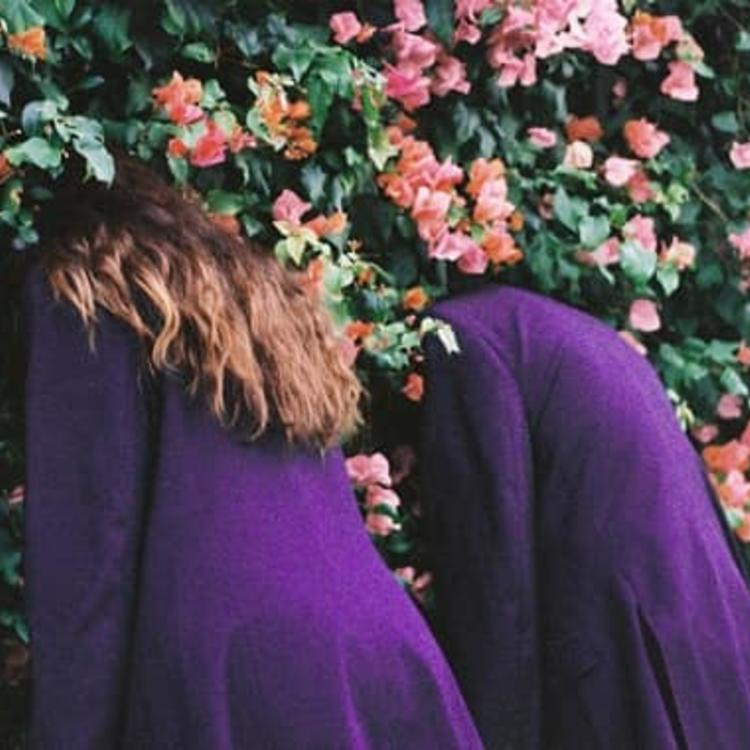 Two people in purple coats with their heads in a bush with pink flowers.