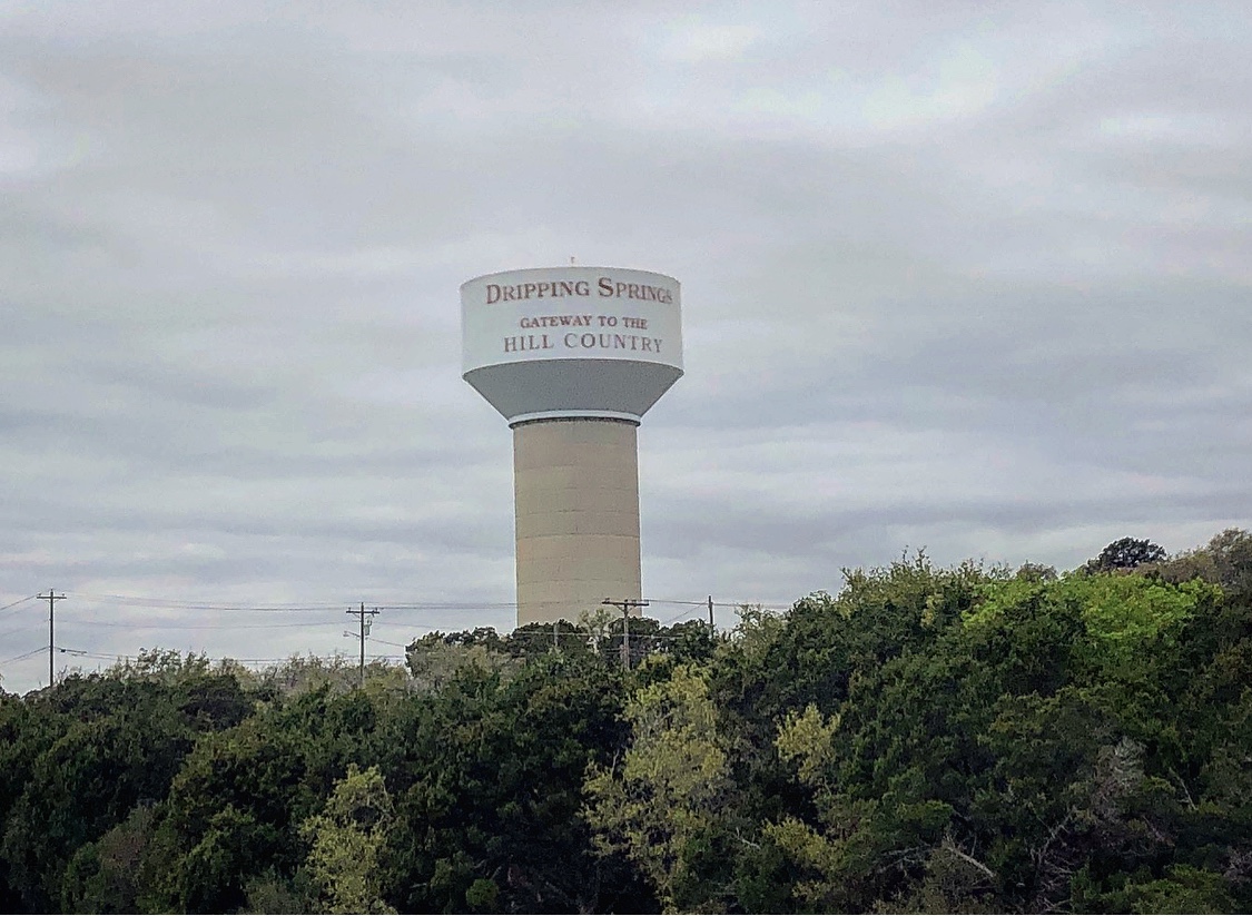 The Dripping Springs water tower surrounded by cloudy skies and green trees.