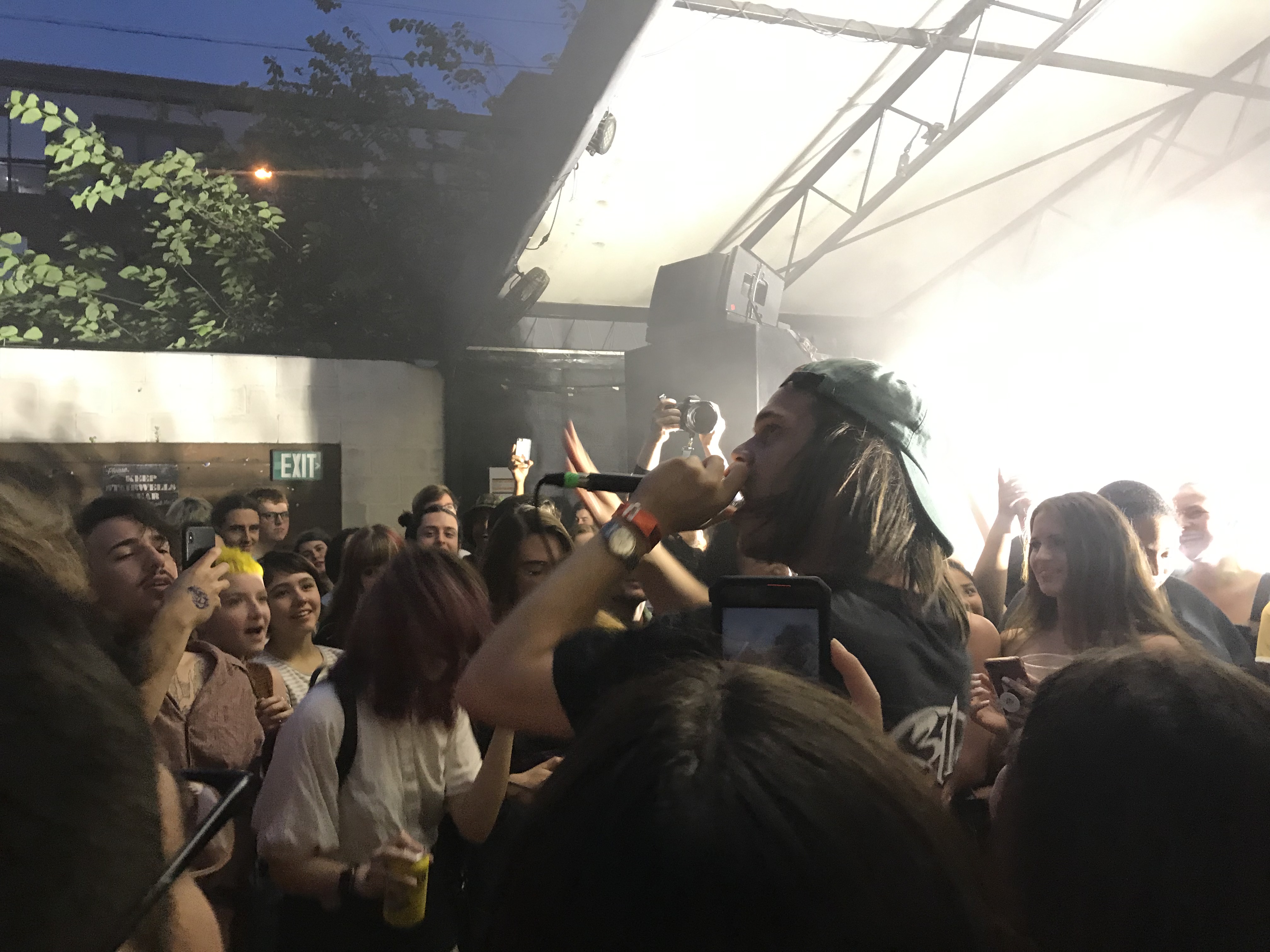 A guy with a hat on singing into a microphone in the middle of the crowd.