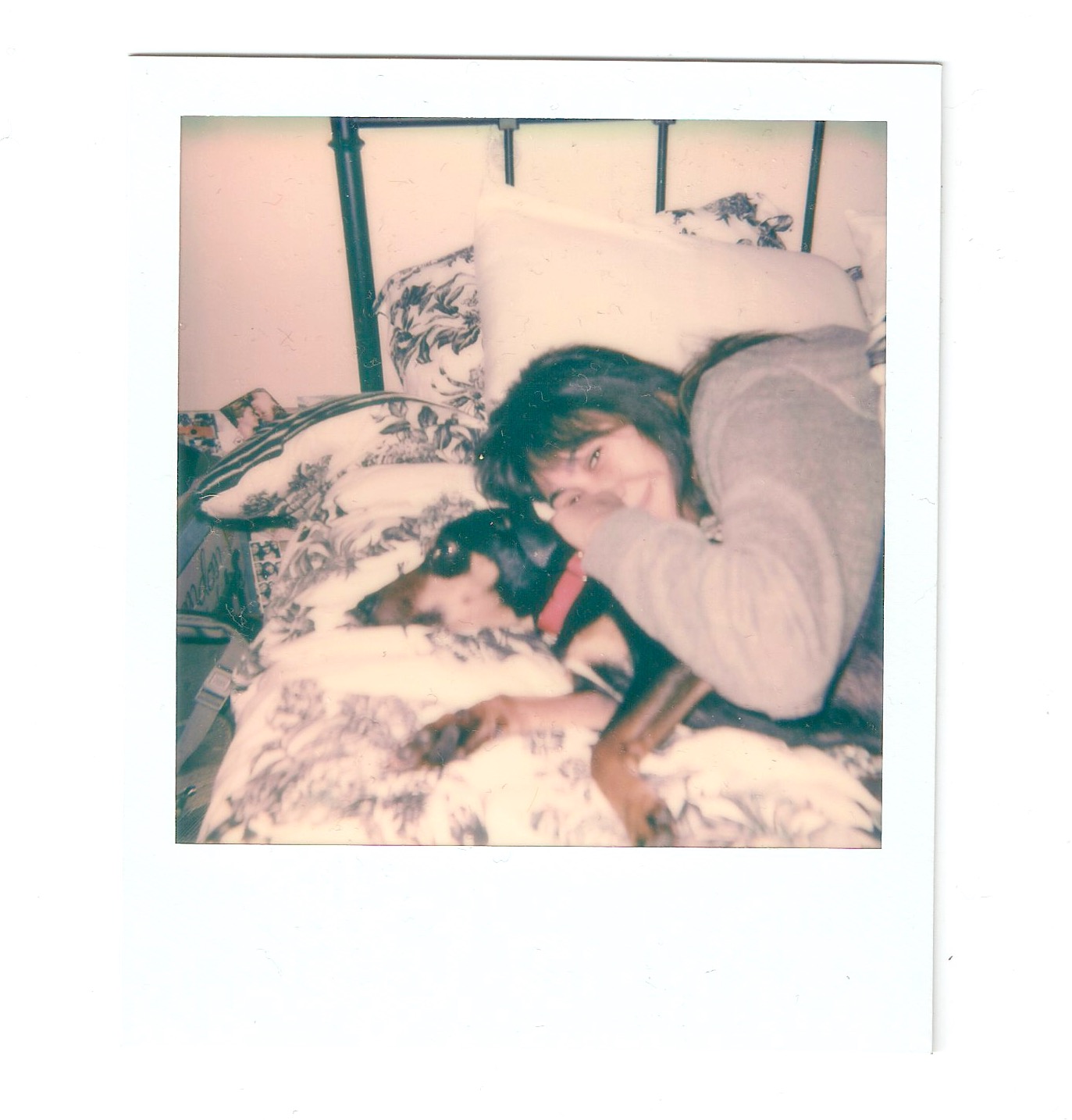 The white framed polaroid photo features a girl laying on a bed with a dog
