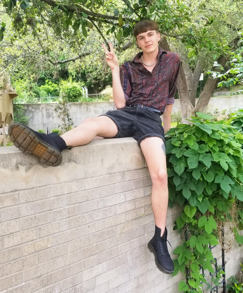A man wearing a purple patterned shirt, sitting on top of a wall.