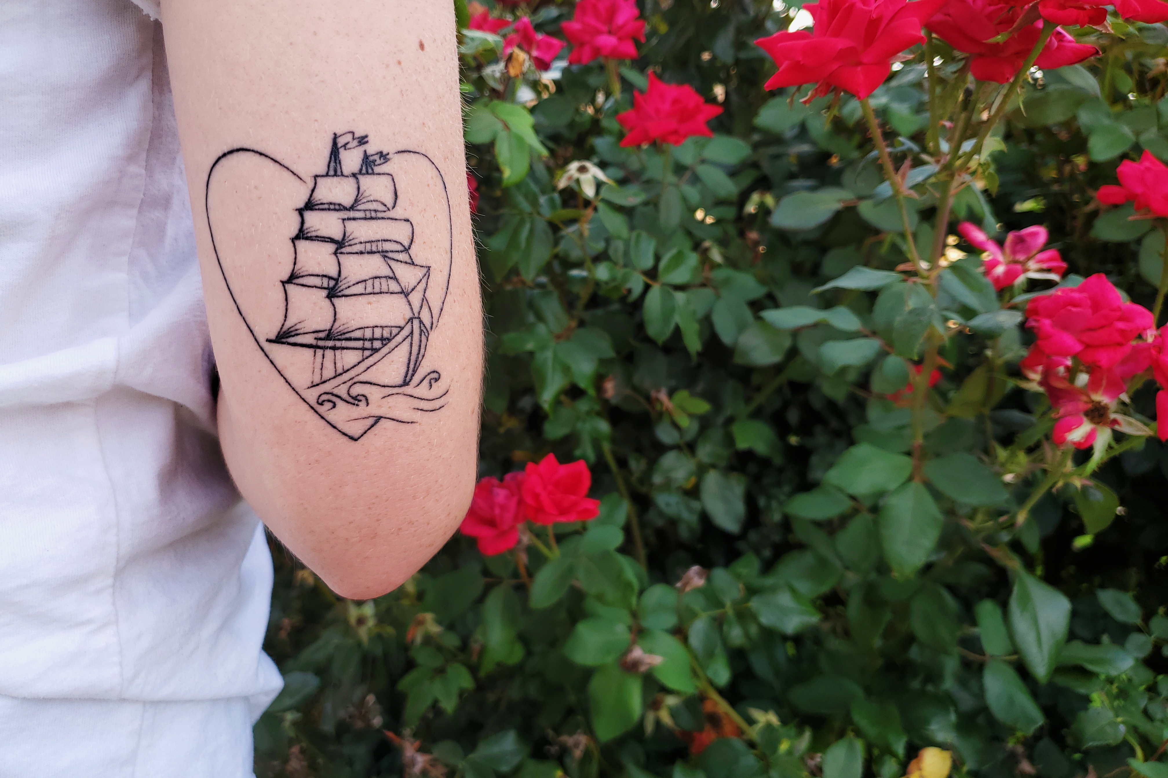 A tattoo on the back of an arm above the elbow of a large ship coming out of a heart.