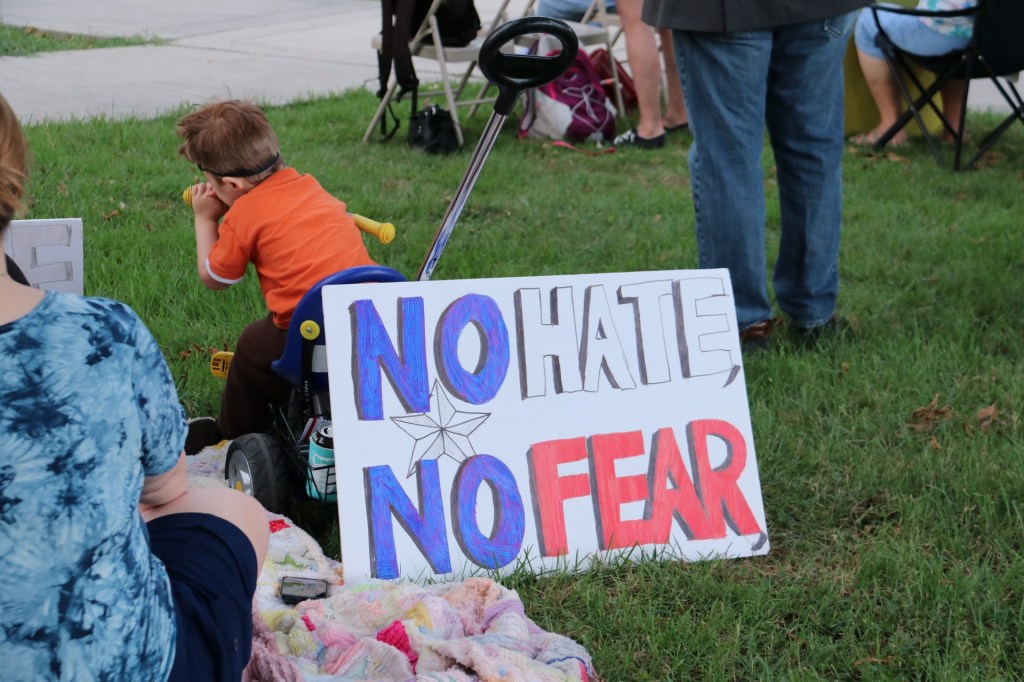 A young child watches from the lawn of the courthouse as a sign reading “no hate no fear” leans on his tricycle.
