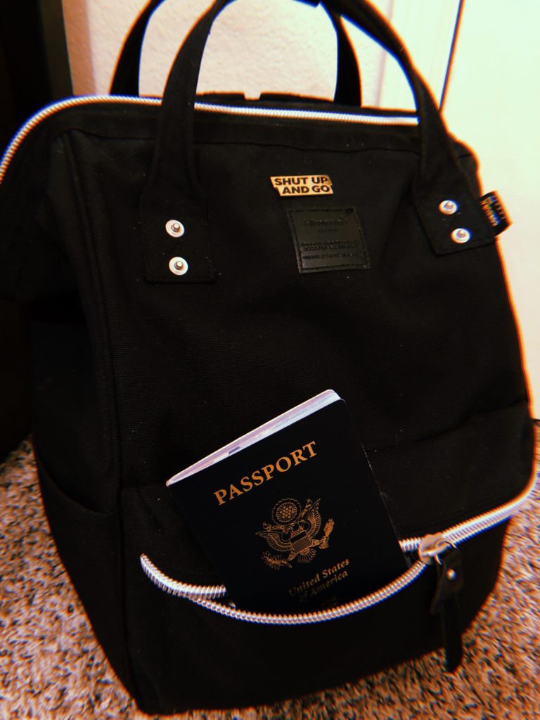 A black backpack with a gold pin and passport sticking out.