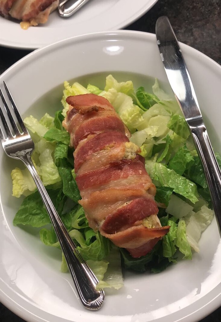 Bacon wrapped chicken on a bed of romaine lettuce with a knife and fork.