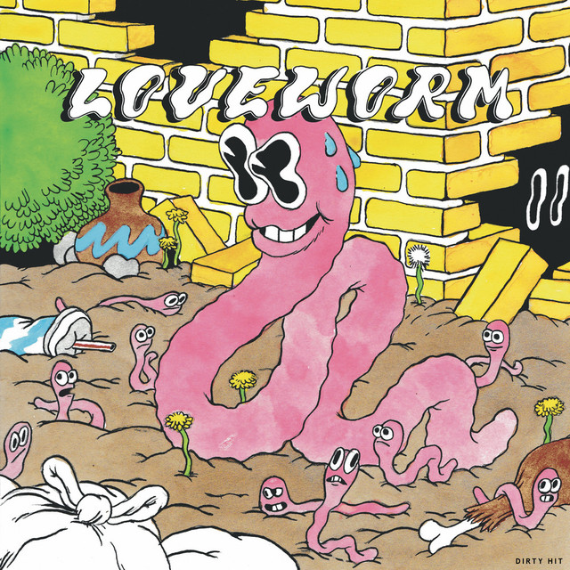 A drawing of several pink earthworms with large eyes sifting through the mud beside a yellow brick wall. The largest worm is smiling and sweating. It has teeth.