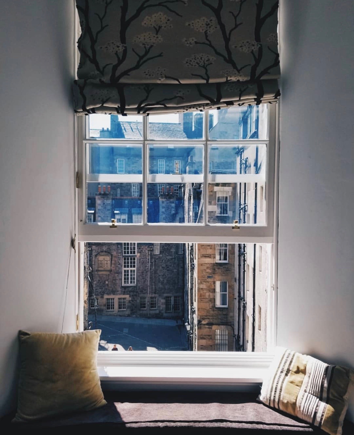 An open window in an Edinburgh flat on a sunny day, with a view into the courtyard and stone buildings across the way.
