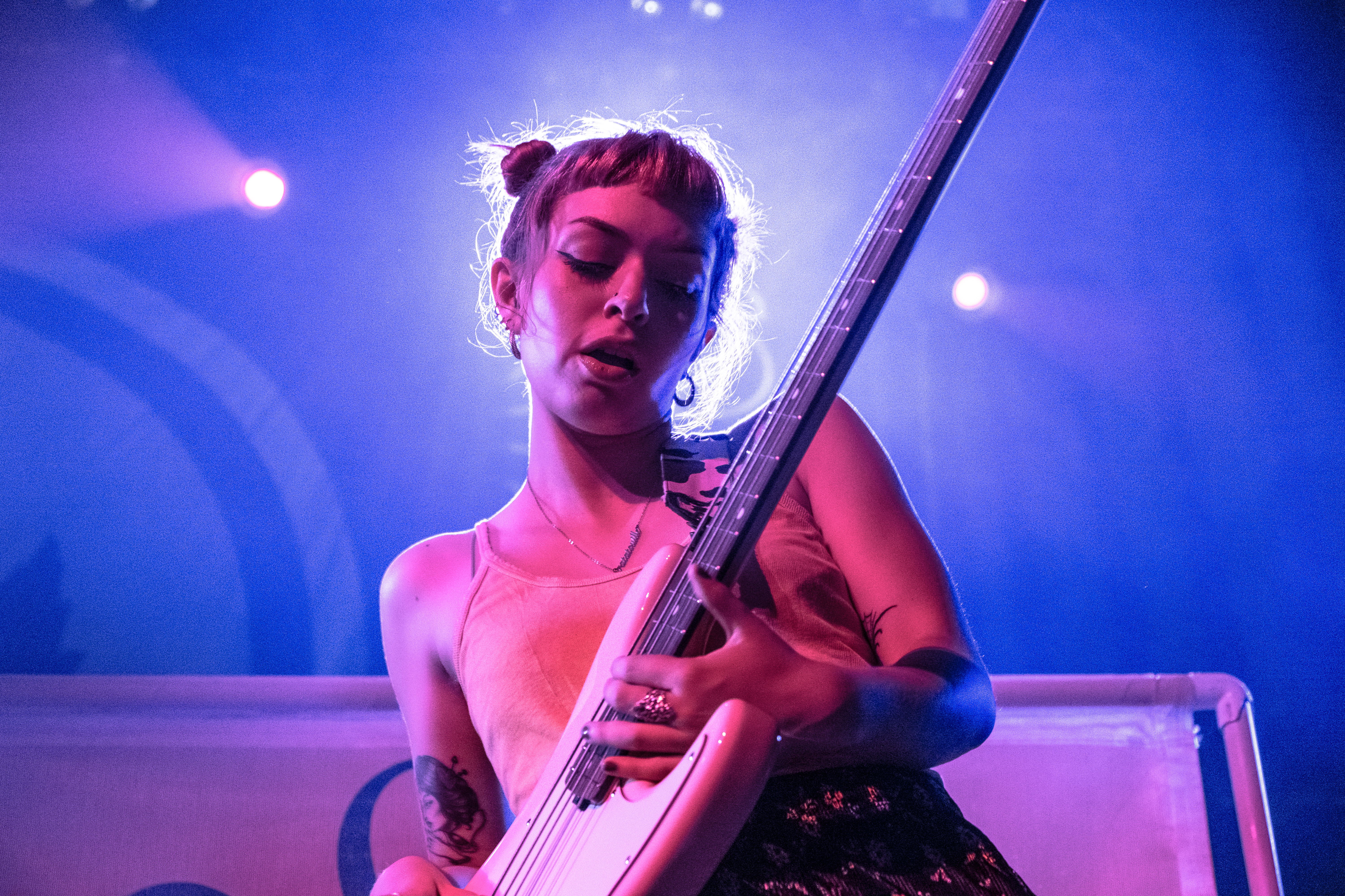 Close up of Doll Skin bassist, Nicole Rich performing on Tuesday night. Rich’s hair is up in two top twist and she is wearing a pink tank top and a floral skirt.