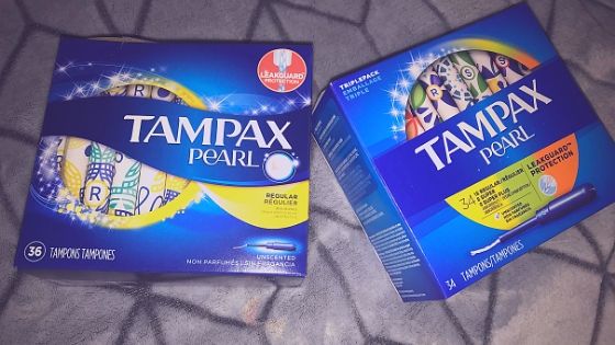 Two blue Tampax Pearl tampon packages on a grey blanket as a background