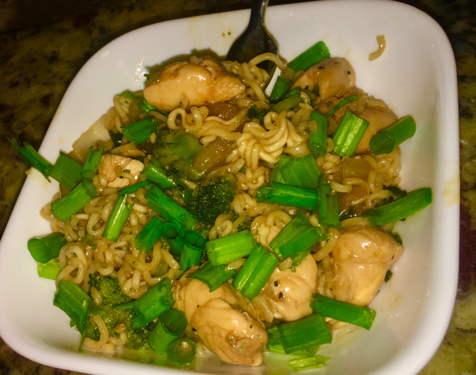 A bowl of teriyaki chicken with noodles and broccoli. Green onions are sprinkled on top.