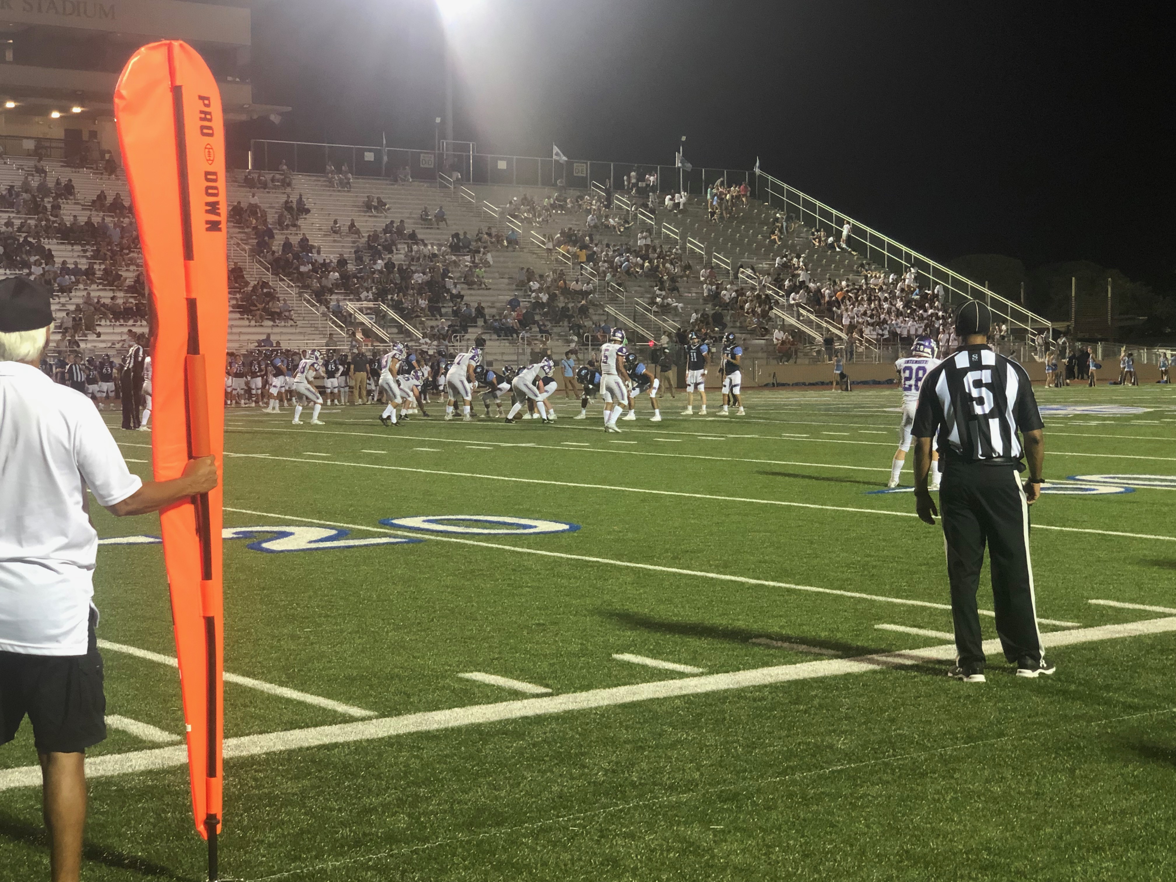 Pre-snap of a Jaguar play on the Rattler 36 yard-line. The Rattler defense is getting set on the line of scrimmage. The first down marker and a referee are visible in the picture watching the play.