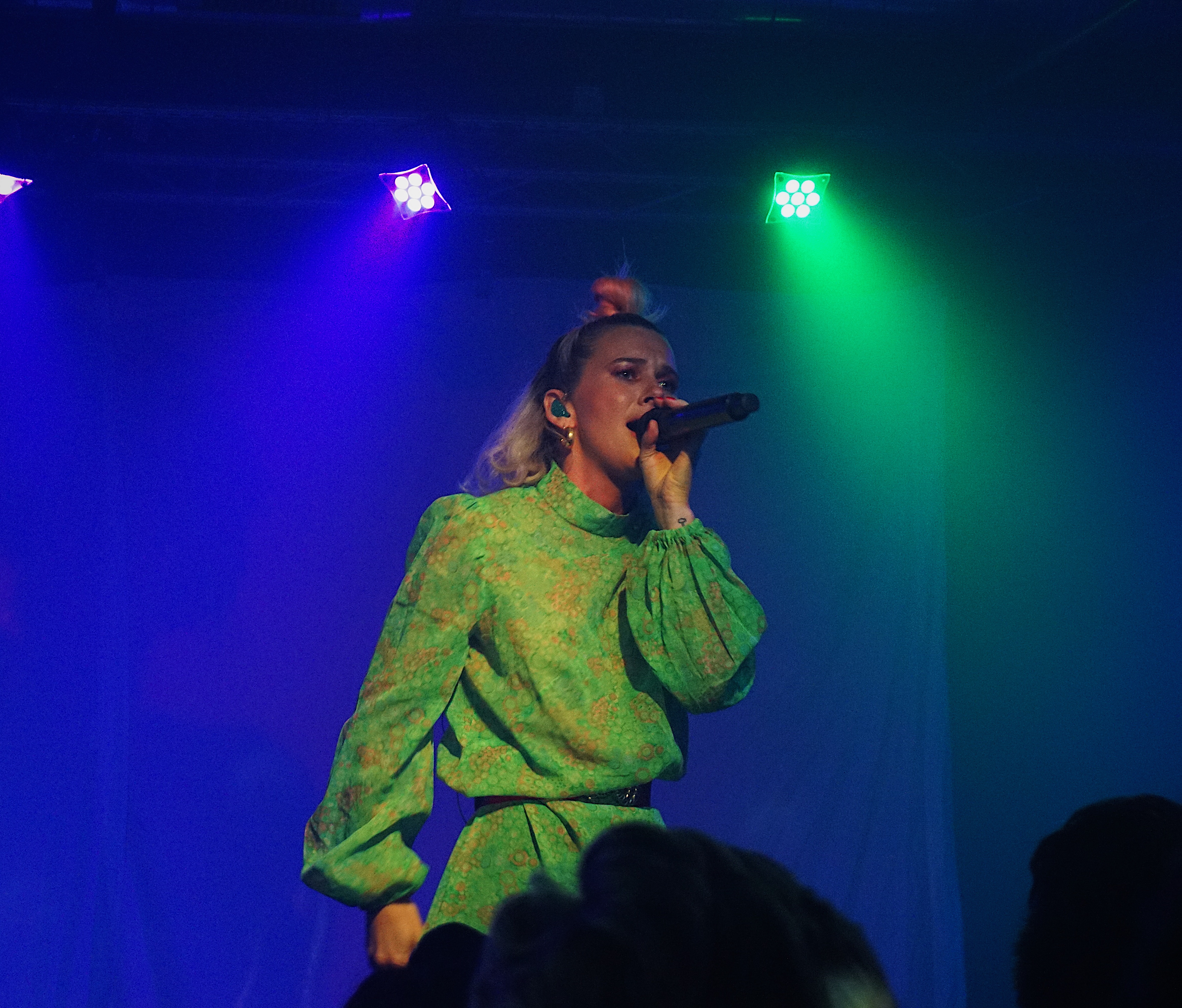 A medium-shot photo of a woman in a green dress holding a microphone in her left hand and singing.
