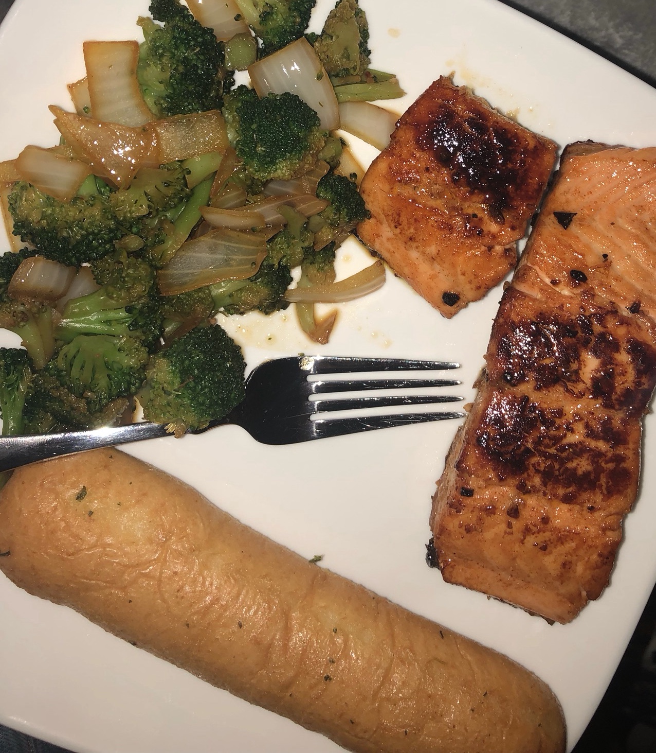 A white plate with salmon, broccoli and garlic bread.
