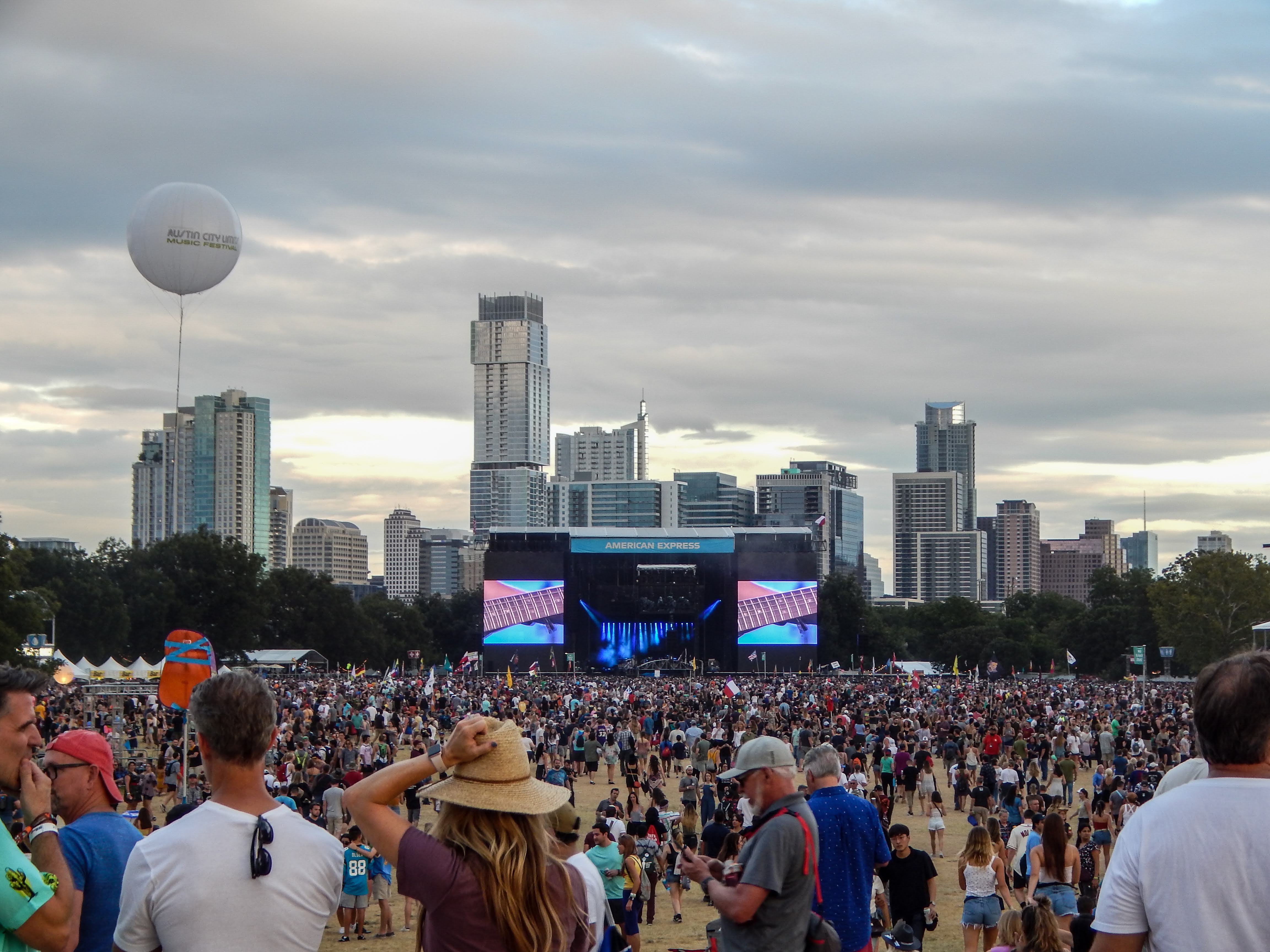 Thousands of people make their way to the biggest stage at Austin City Limits. You can see the Austin skyline behind the stage.
