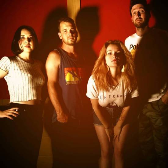 Shot of the four members of Black Basements, with deep shadows, standing in front of a dark red wall.