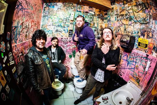 The members of Gold Leather are posing in an empty bathroom with heavily graffitied walls.