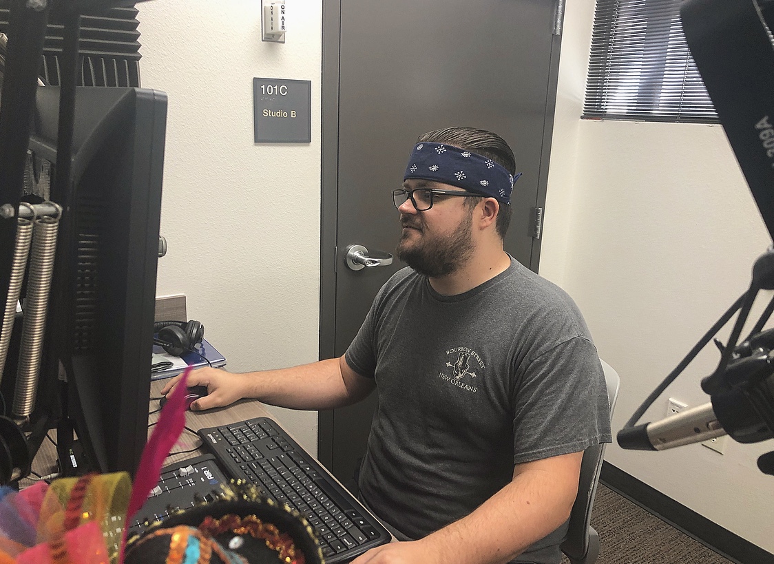 Man wearing a navy bandana and gray tshirt sits at desk looking at a computer.