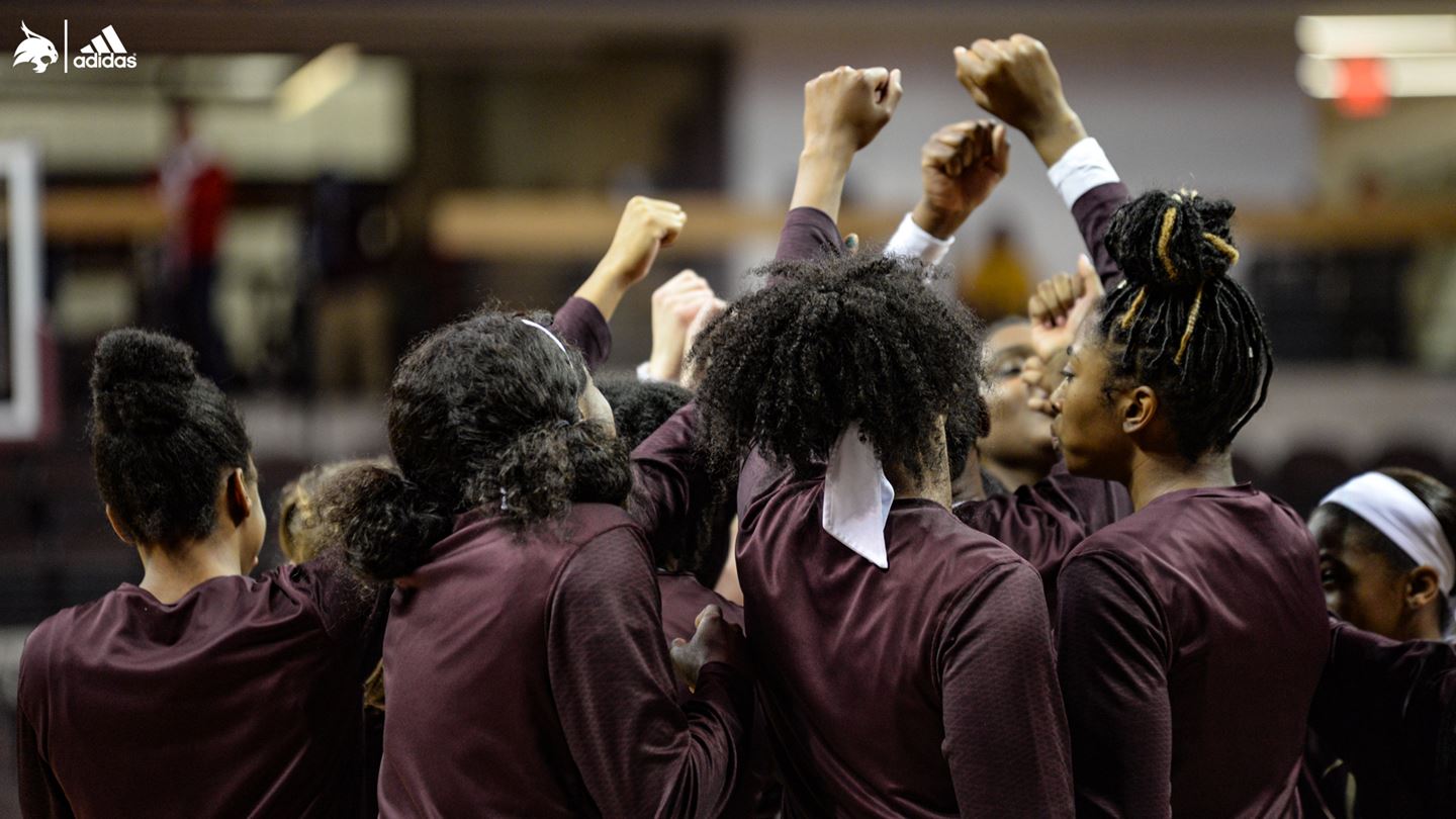 Women in Maroon Texas State shirts raise their hands together to break out of a huddle.