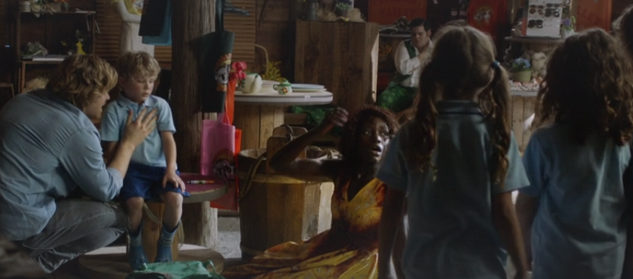 Mrs. Caroline sits on the floor in a yellow dress covered in blood in front of her students. Behind her Dave hugs his nephew who just had an allergic reaction.