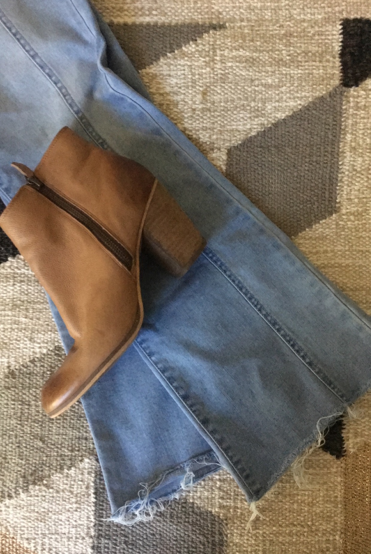 A pair of light pants laying on a background with a brown bootie sitting in the top of the photo frame.