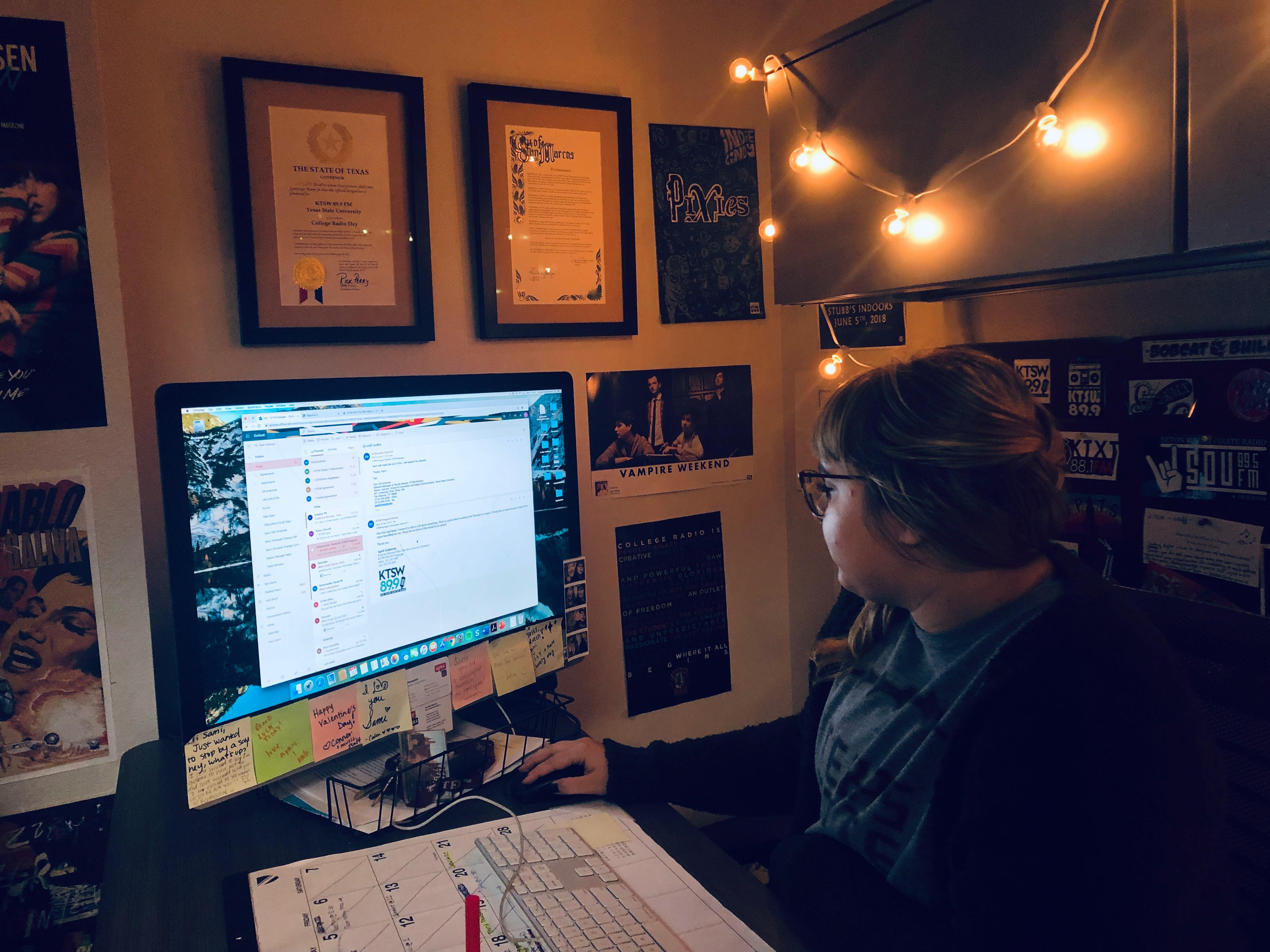 Sami responding to emails in her office with posters on the wall and hanging lights