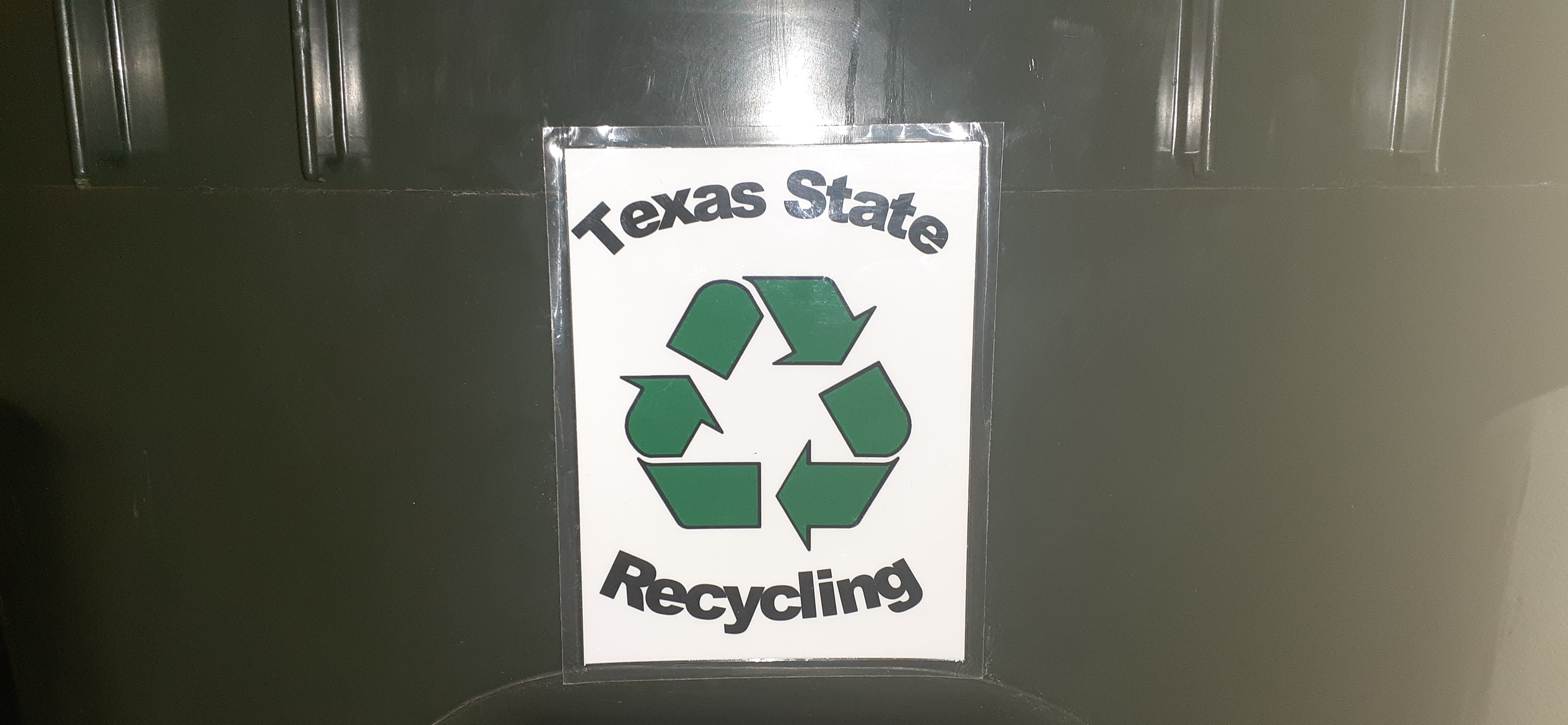 Green trash can with a recycling tag that says Texas State Recycling in black with a white paper background