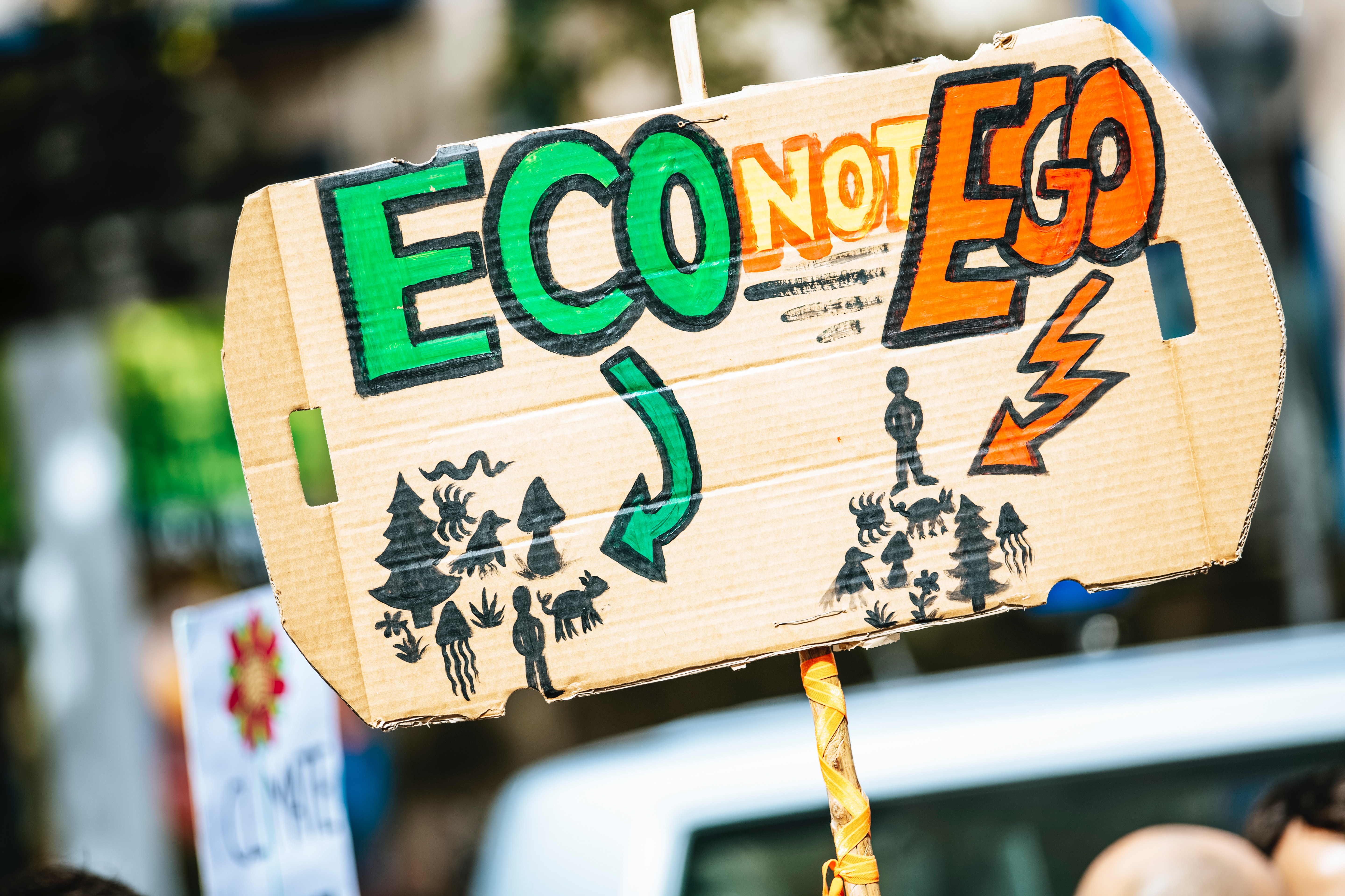 A cardboard sign with the phrase “Eco not ego” painted on it