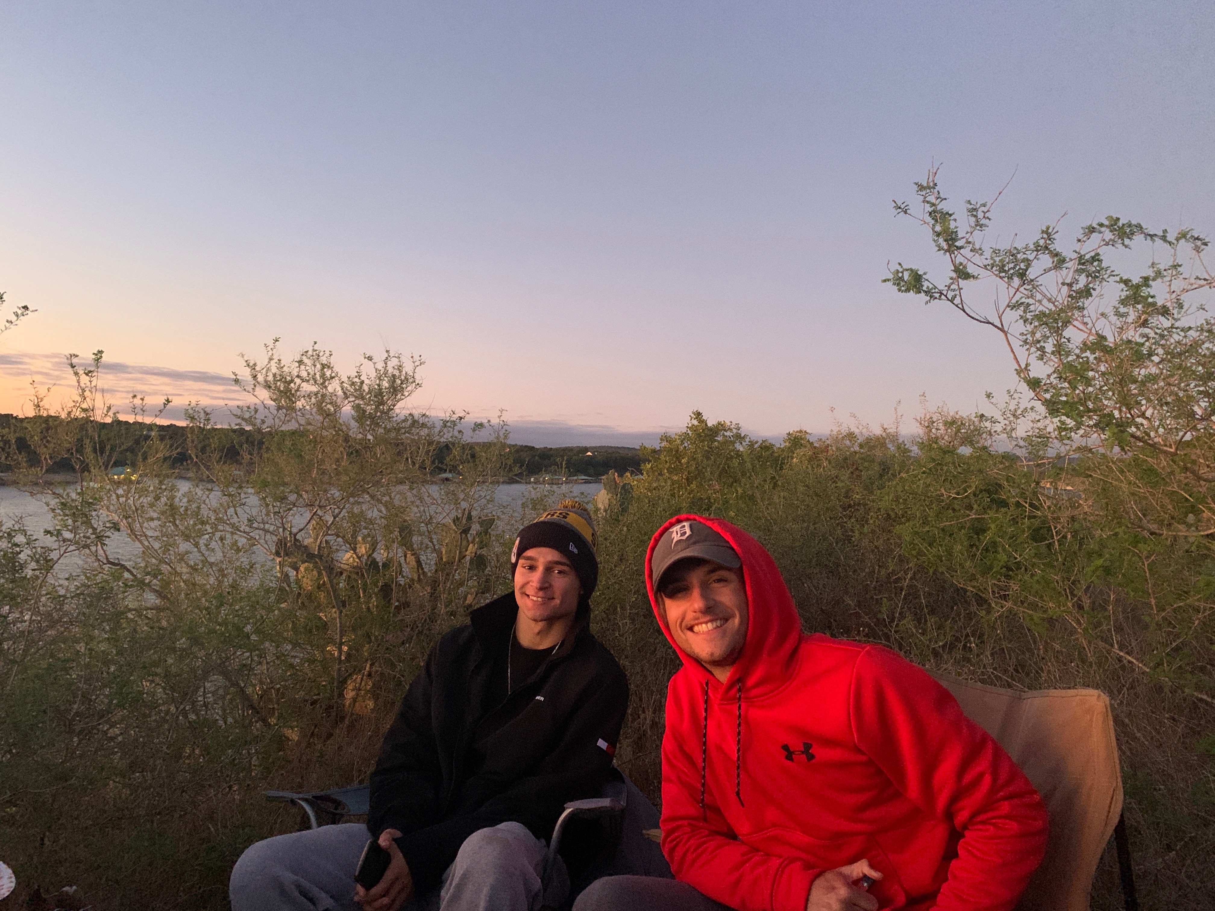 Two men sit in lawn chairs on a cliff with a sunset in the background.