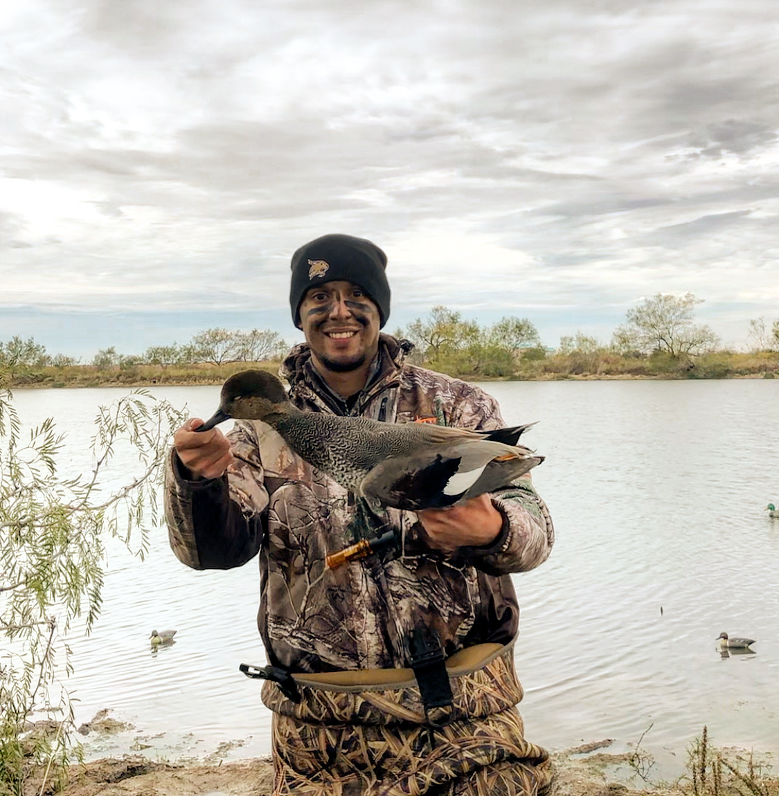 Jacob stands in a field with camouflage on holding a duck.