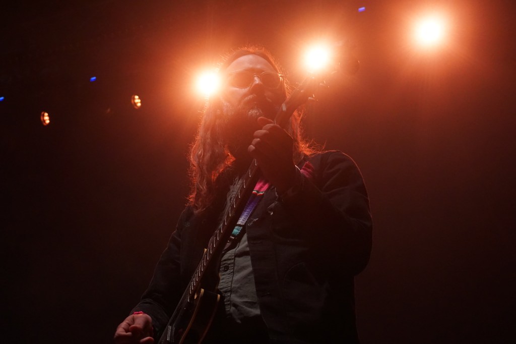 The guitarist of Israel Nash washed out by the orange stage lights strumming away in the night.