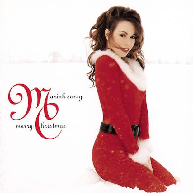 Mariah Carey sits on a white background while wearing Santa’s outfit.
