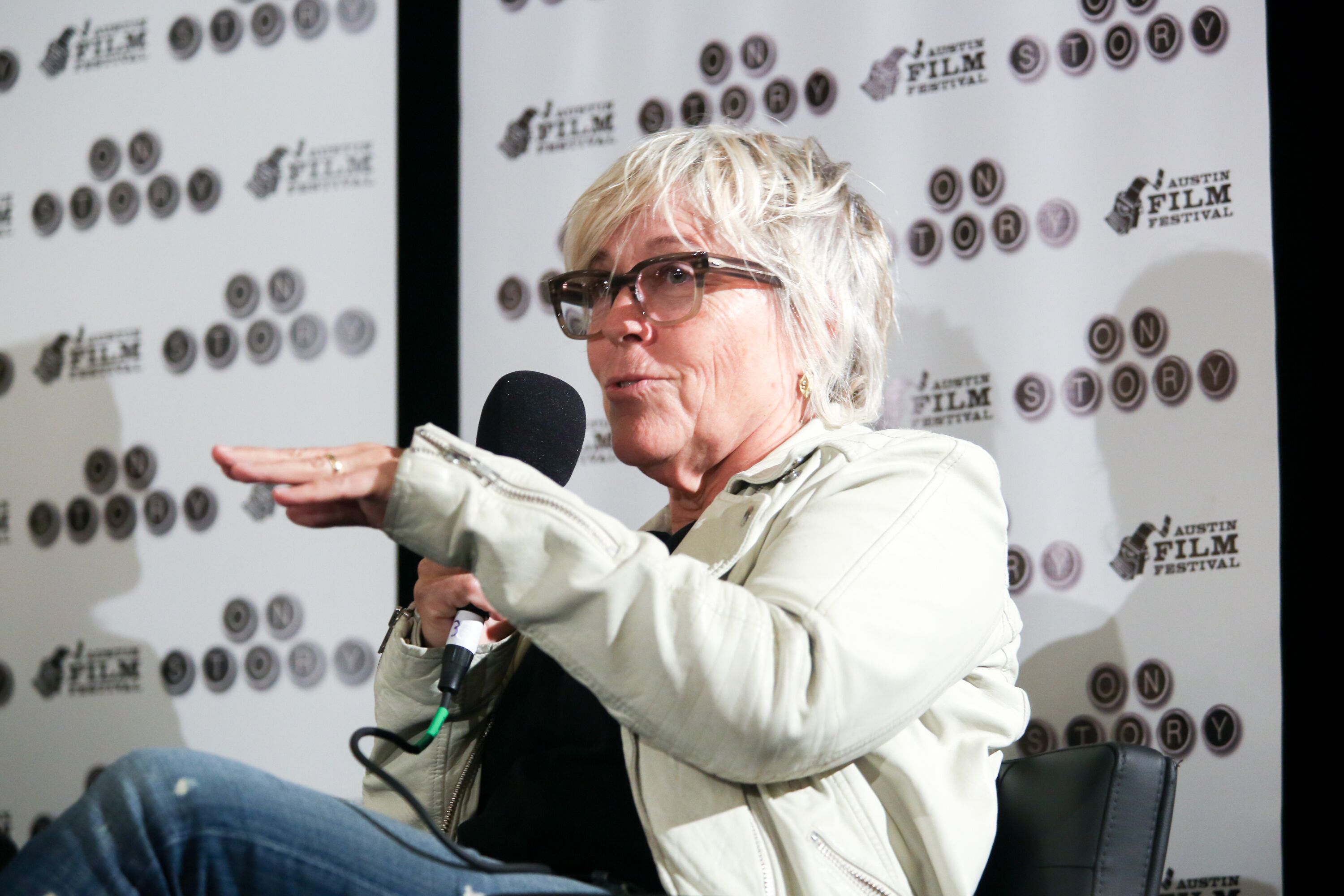 A woman with black glasses holds a microphone on stage