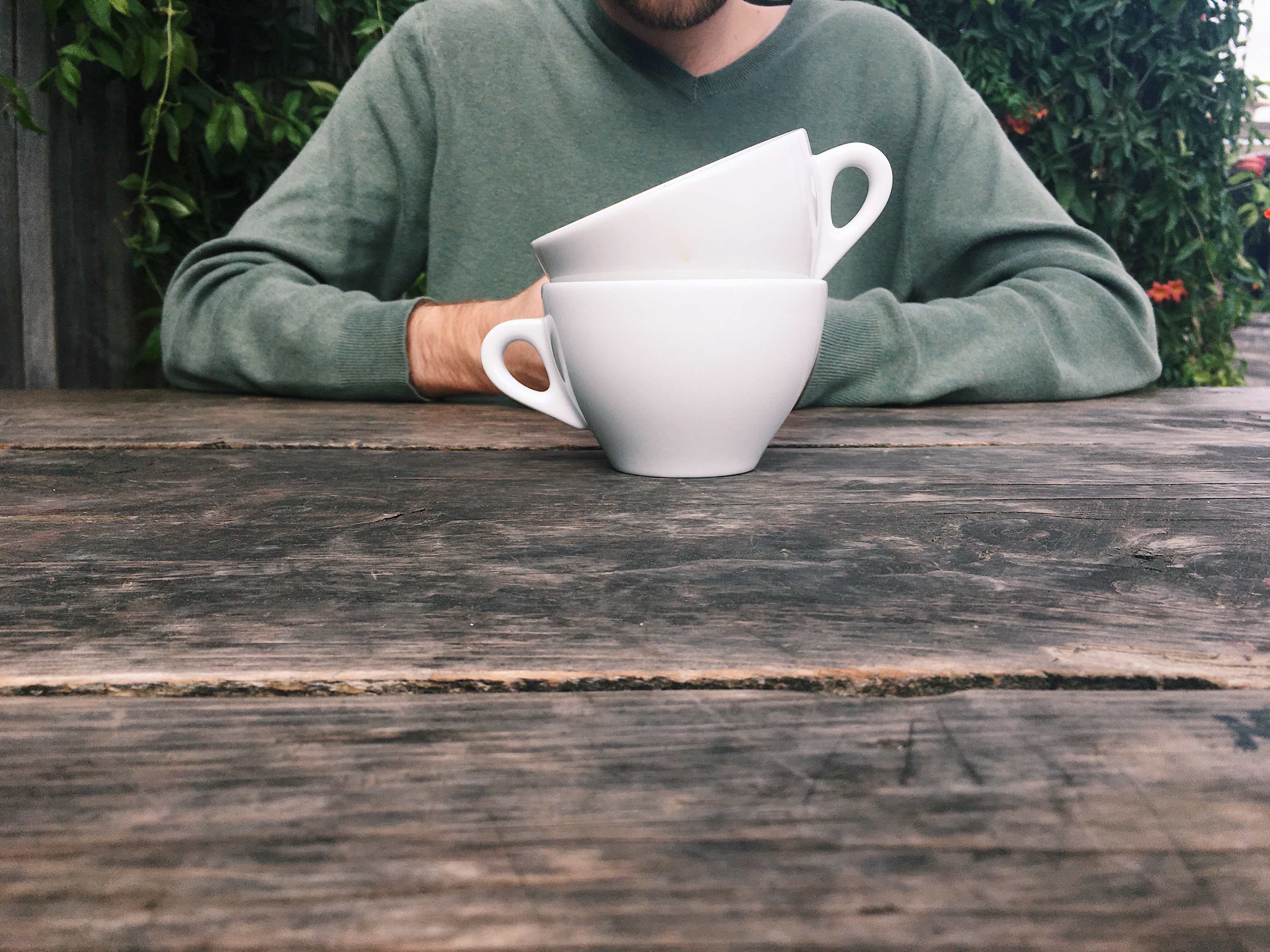 A man in a green sweater sitting behind two stacked coffee mugs.
