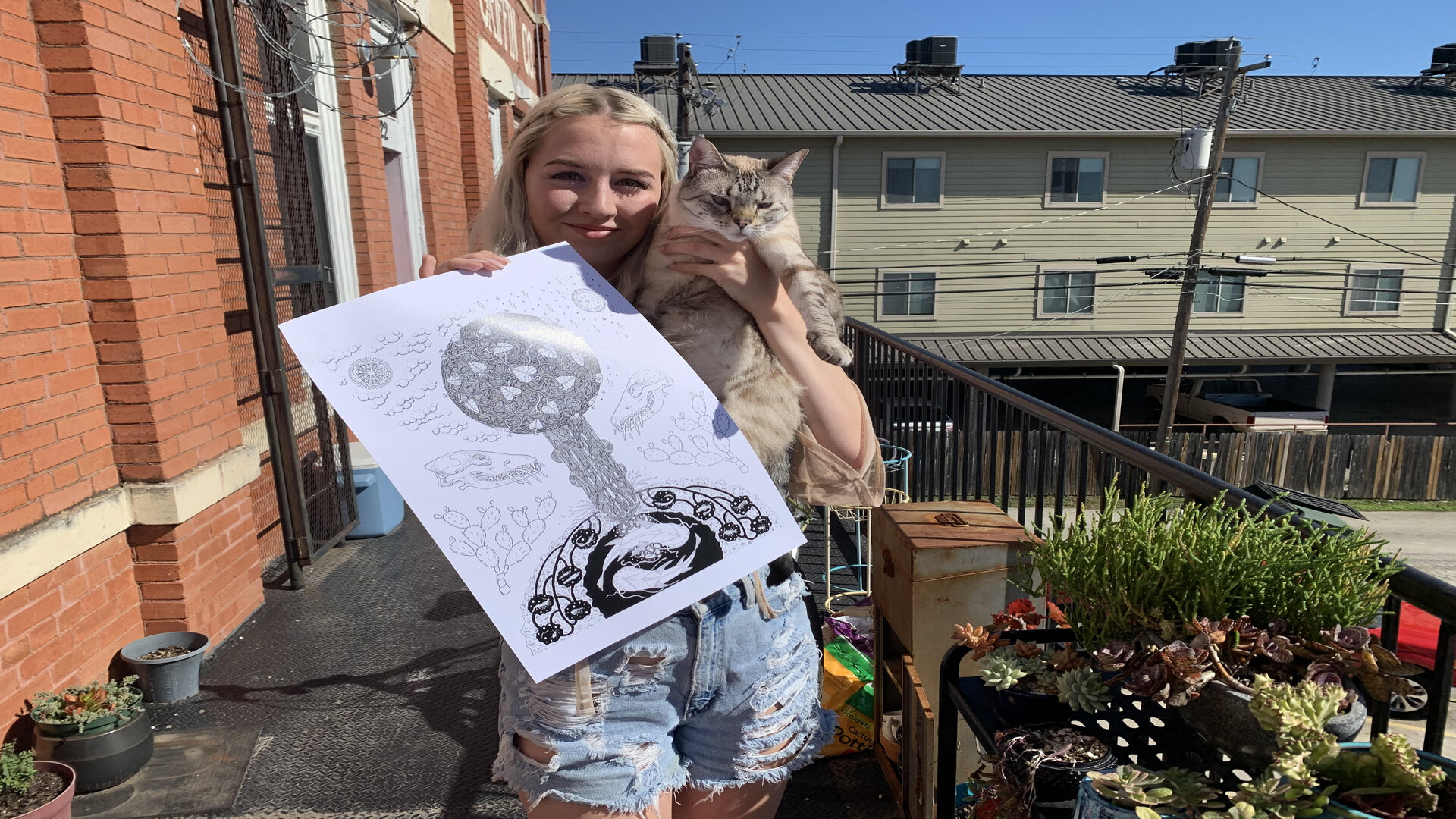 Phoebe Mau outside holding one of her art pieces and her cat, Mika