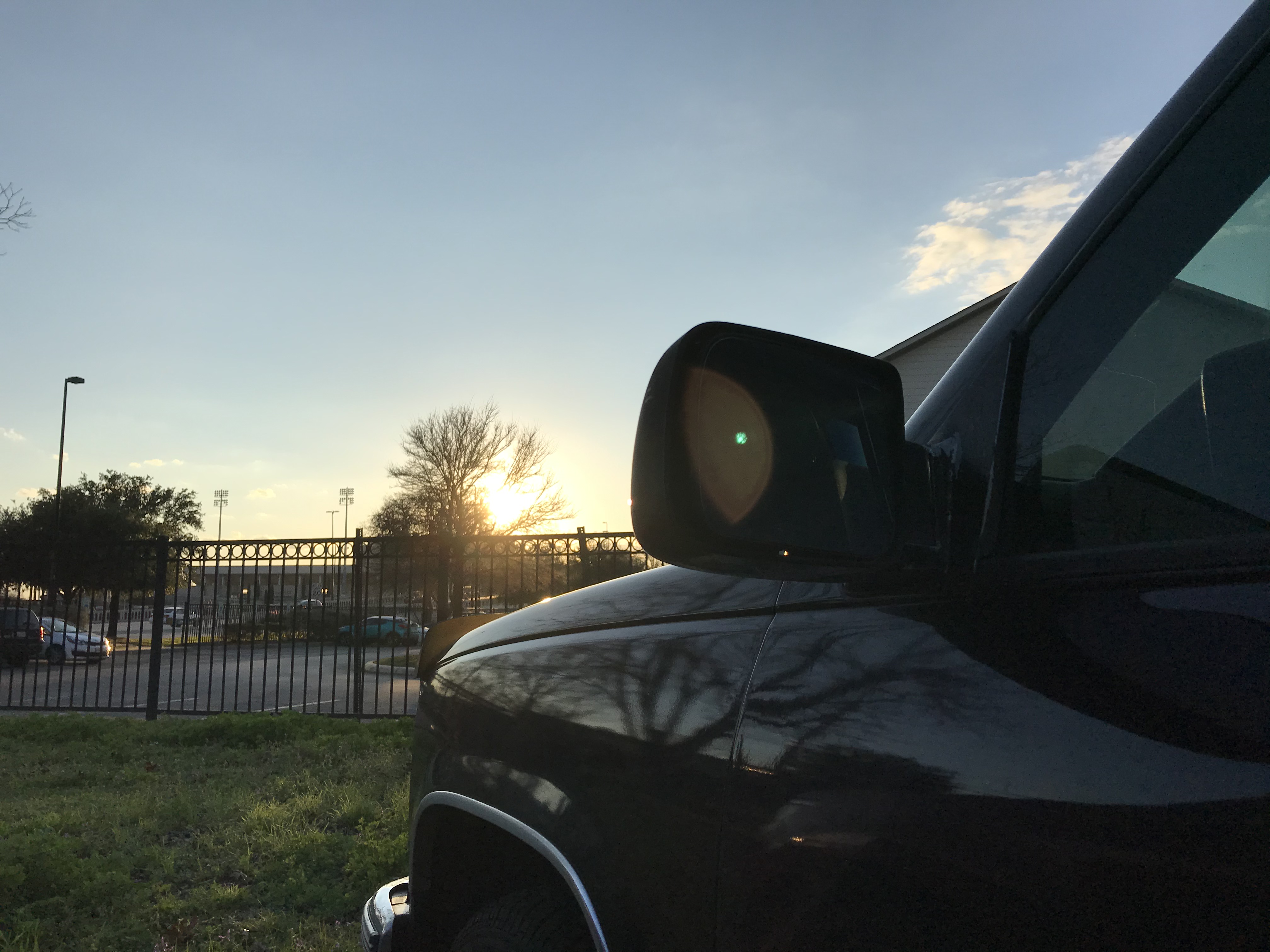 The front of a truck sits off to the right; a building behind it blocks some of the sun's setting rays.