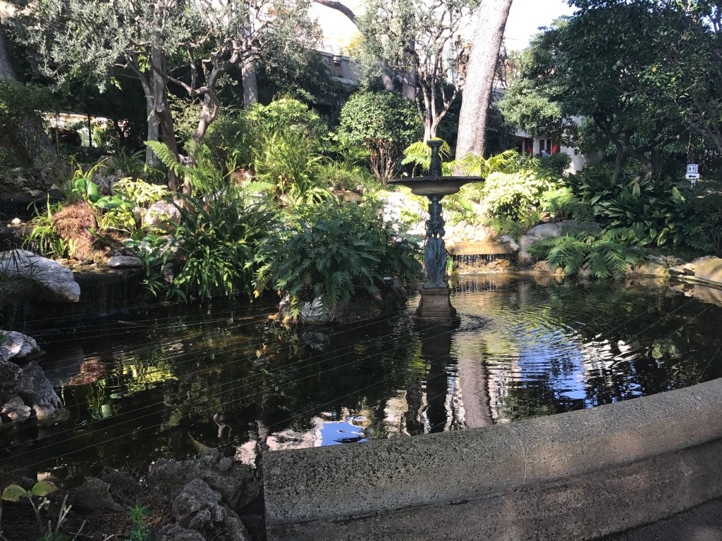 a statue of two people standing in the middle of a fountain in a garden