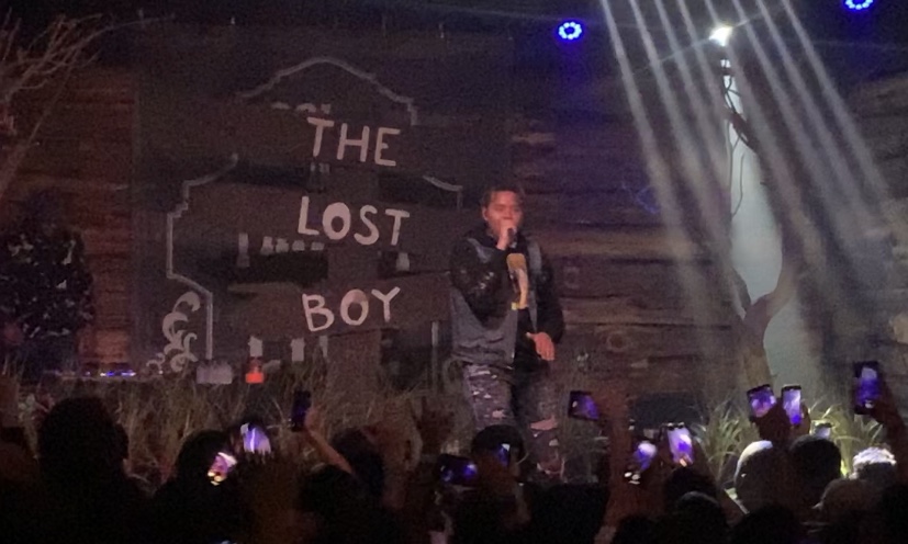 YBN Cordae performing in front of a crowd with a sign behind him that says The Lost Boy