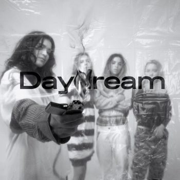 Black and white image of The Aces standing across the horizon line of the image. One of the girls is holding a lighter in full flame in front of the camera and the word “Daydream” is spelled out in the center.