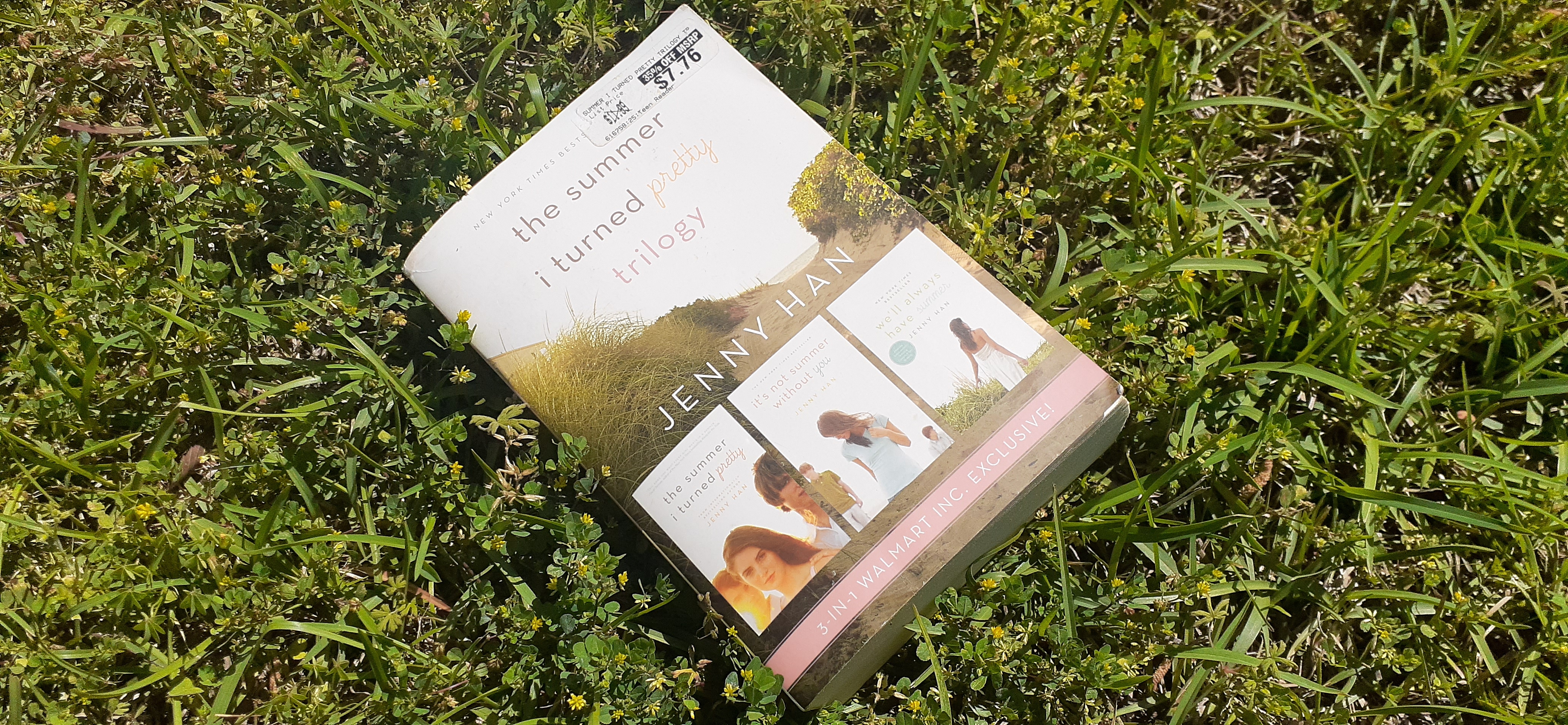 a big white book with a girl and two boys on the cover lies in the grass in the sun