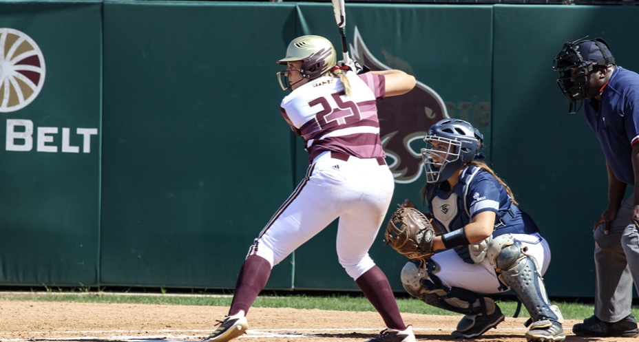 MacKay is up to bat wearing her maroon and white uniform with her gold helmet seconds away from swinging her bat