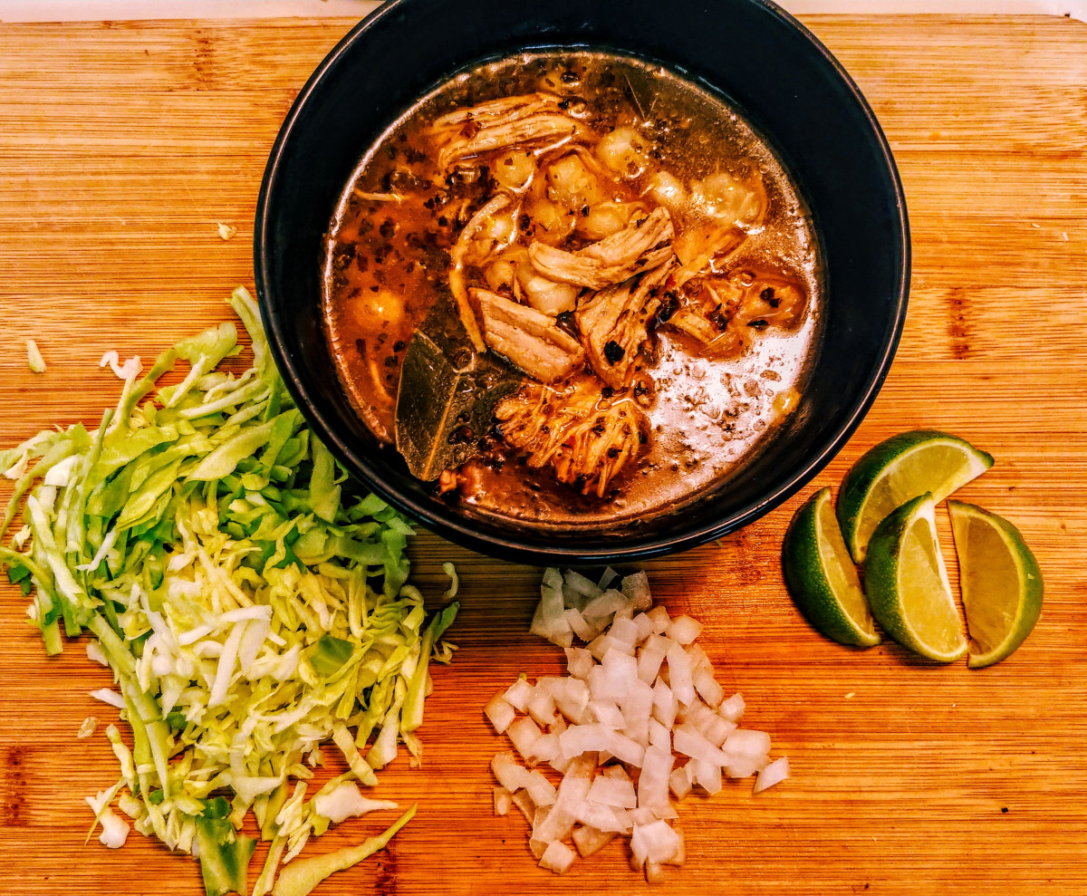 Limes, Onions,Lettuce, Chicken all placed around and in a black bowl on a brown wood table.
